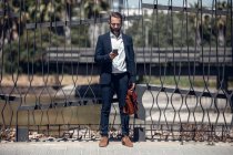 Бизнесмен использует мобильный телефон, стоя перед забором — стоковое фото