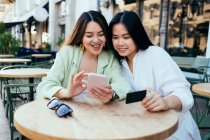 Lächelnde Frauen kaufen online per Smartphone im Bürgersteig-Café ein — Stockfoto
