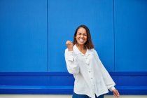 Joyeux jeune femme acclamant devant le mur bleu — Photo de stock