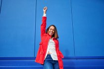 Femme heureuse avec la main levée debout devant le mur bleu — Photo de stock