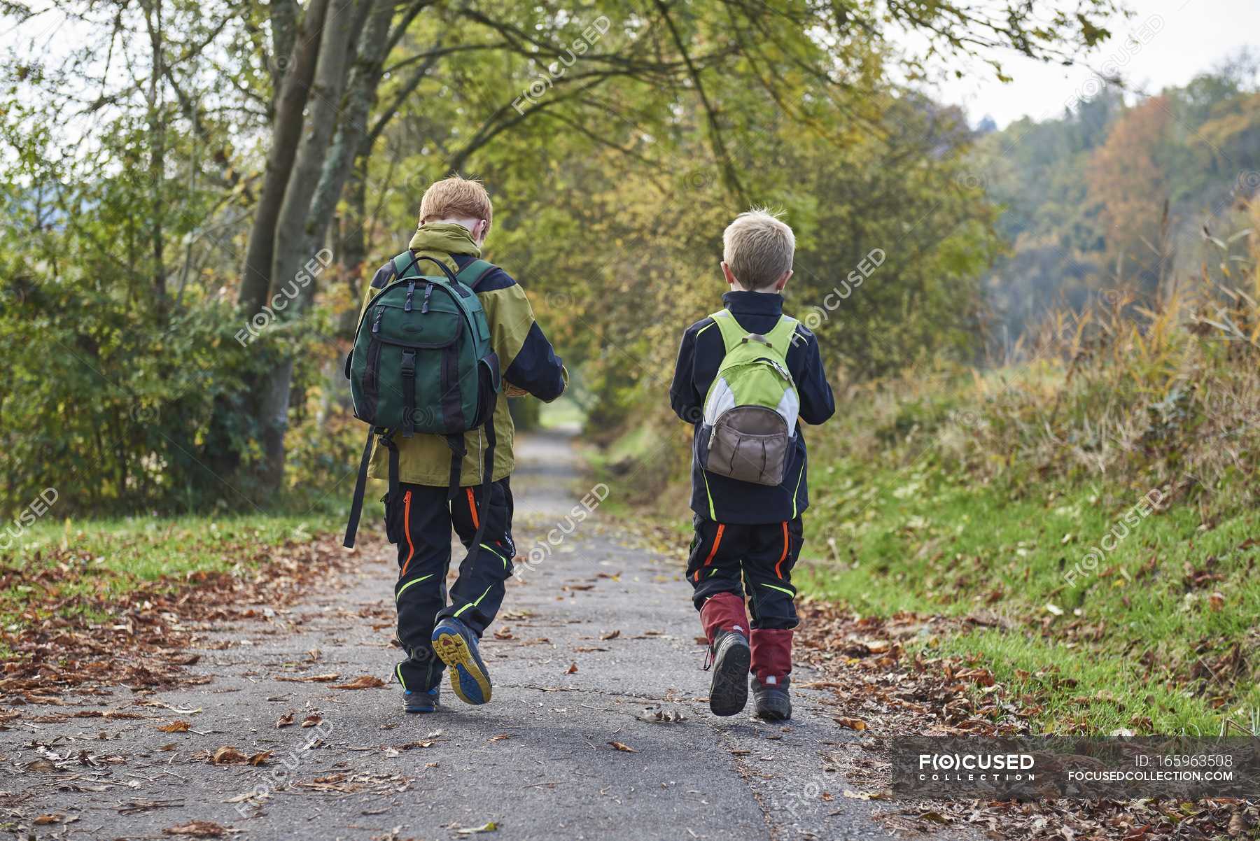 Two boys walking through forest with backpacks, rear view — best friends,  Strolling - Stock Photo | #165963508