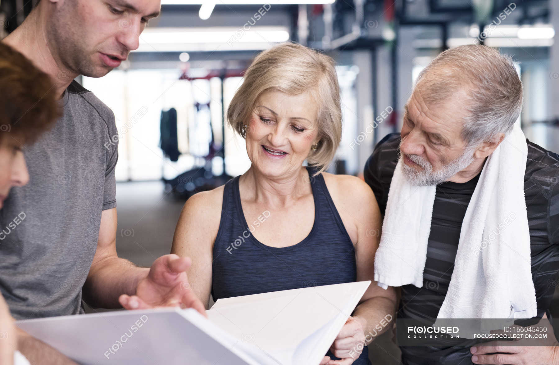 Seniors And Personal Trainer Looking In Folder Well Being Discussing   Focused 166045450 Stock Photo Seniors And Personal Trainer Looking 