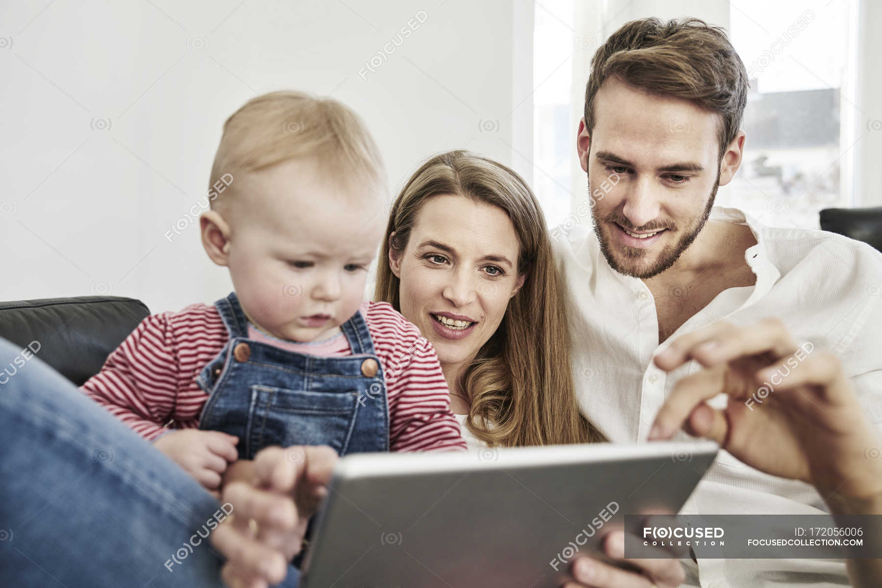 Parents With Baby Girl Looking At Tablet On Couch Indoors Two Parents Stock Photo