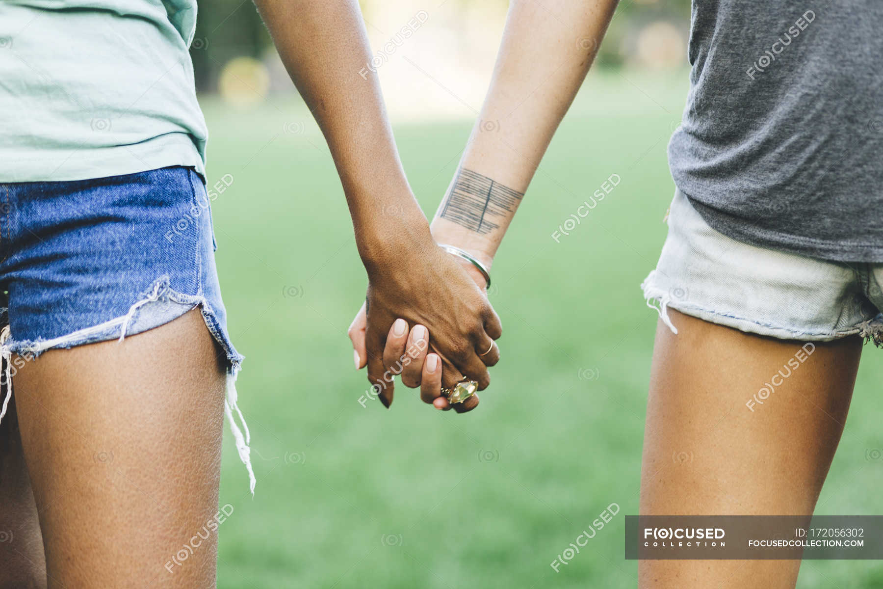 Close-up of Two women holding hands in a park — friends, tattoo - Stock