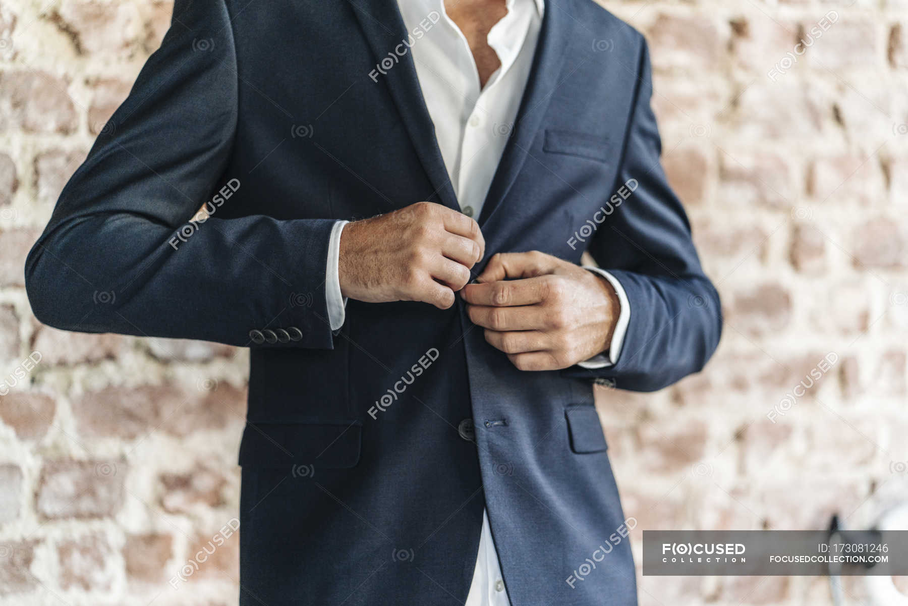 Close Up Of Businessman Buttoning Jacket In Front Of Brick Wall — Male