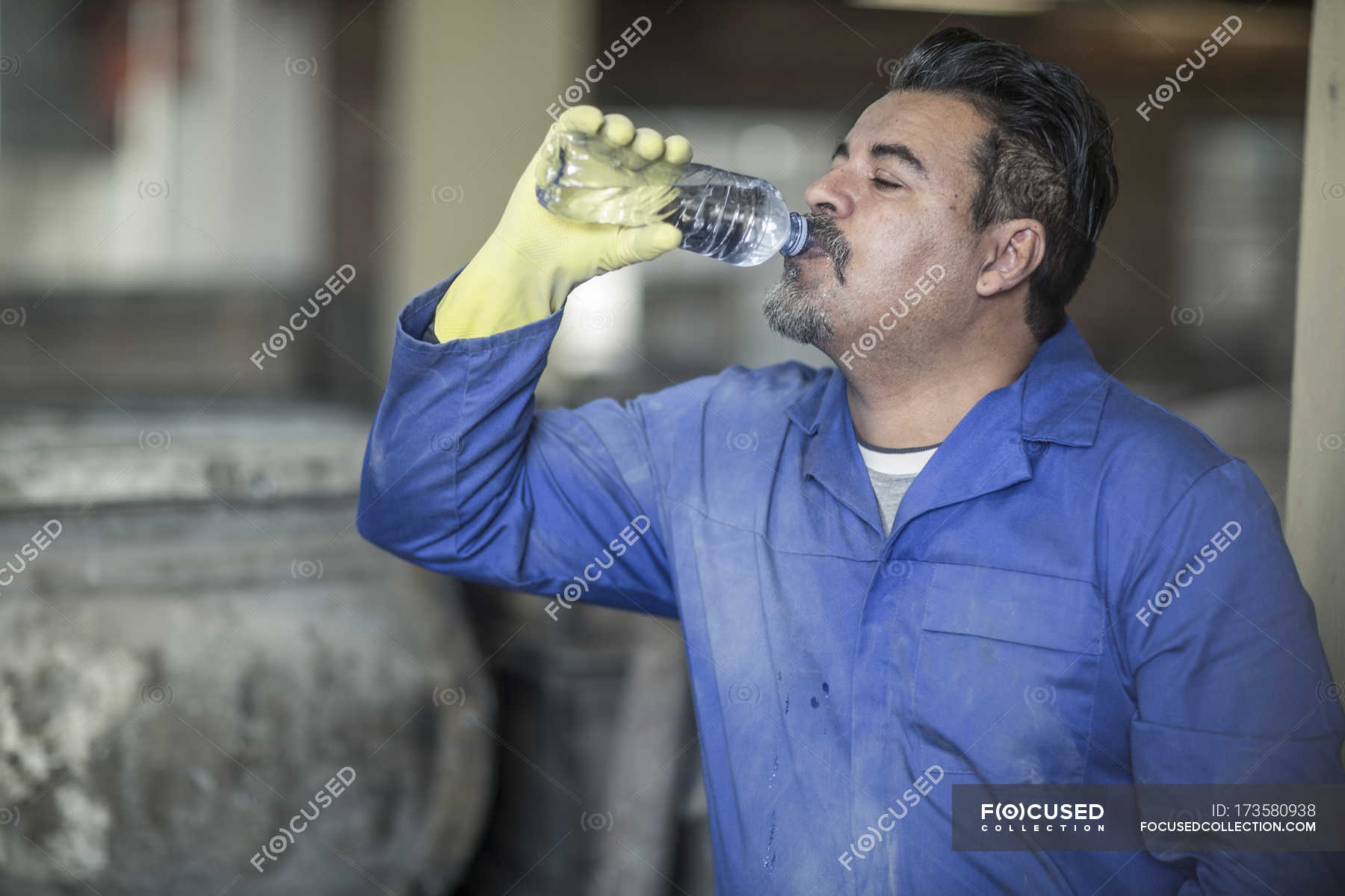 Worker drinking water from bottle in industrial factory — protective ...