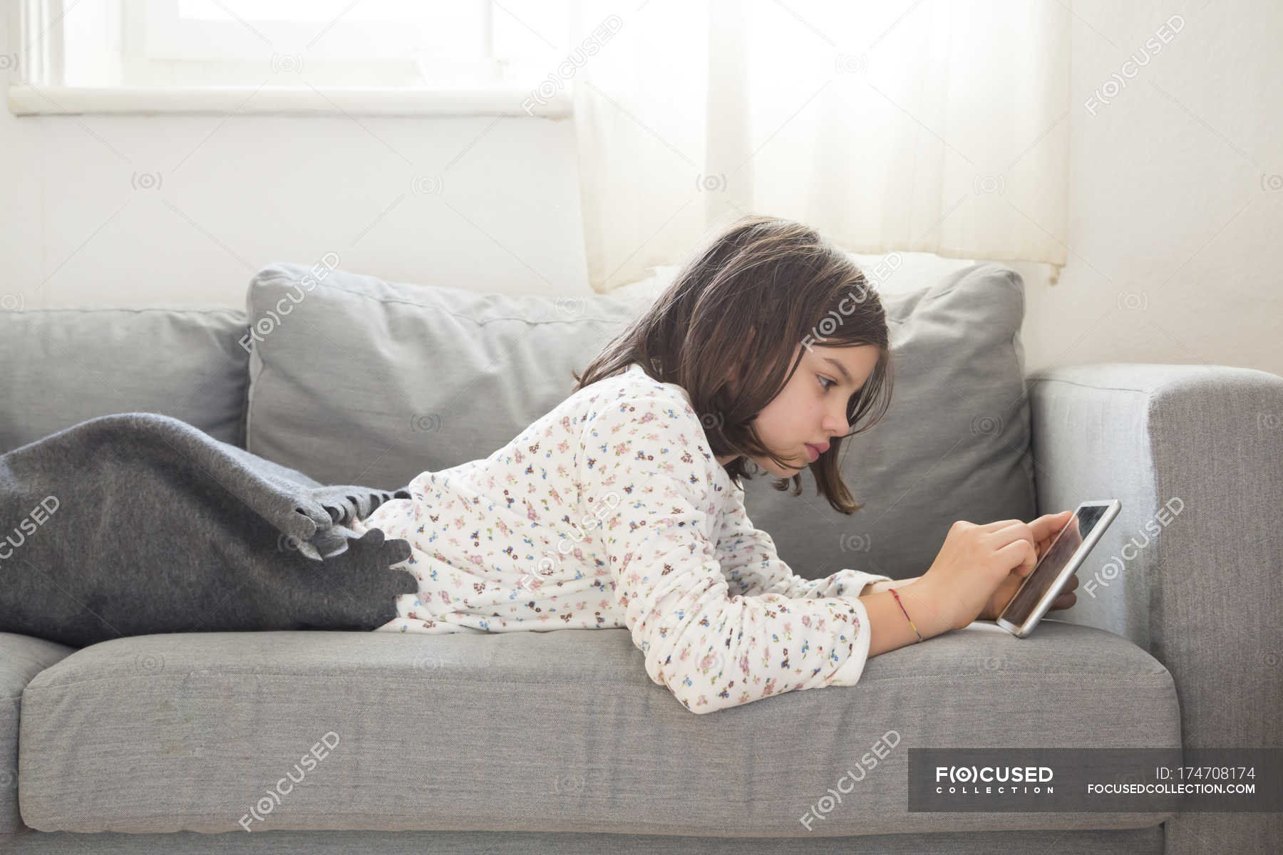 Девушка лежит на диване и с помощью мини-планшета — Досуг, Вид сбоку -Stock Photo