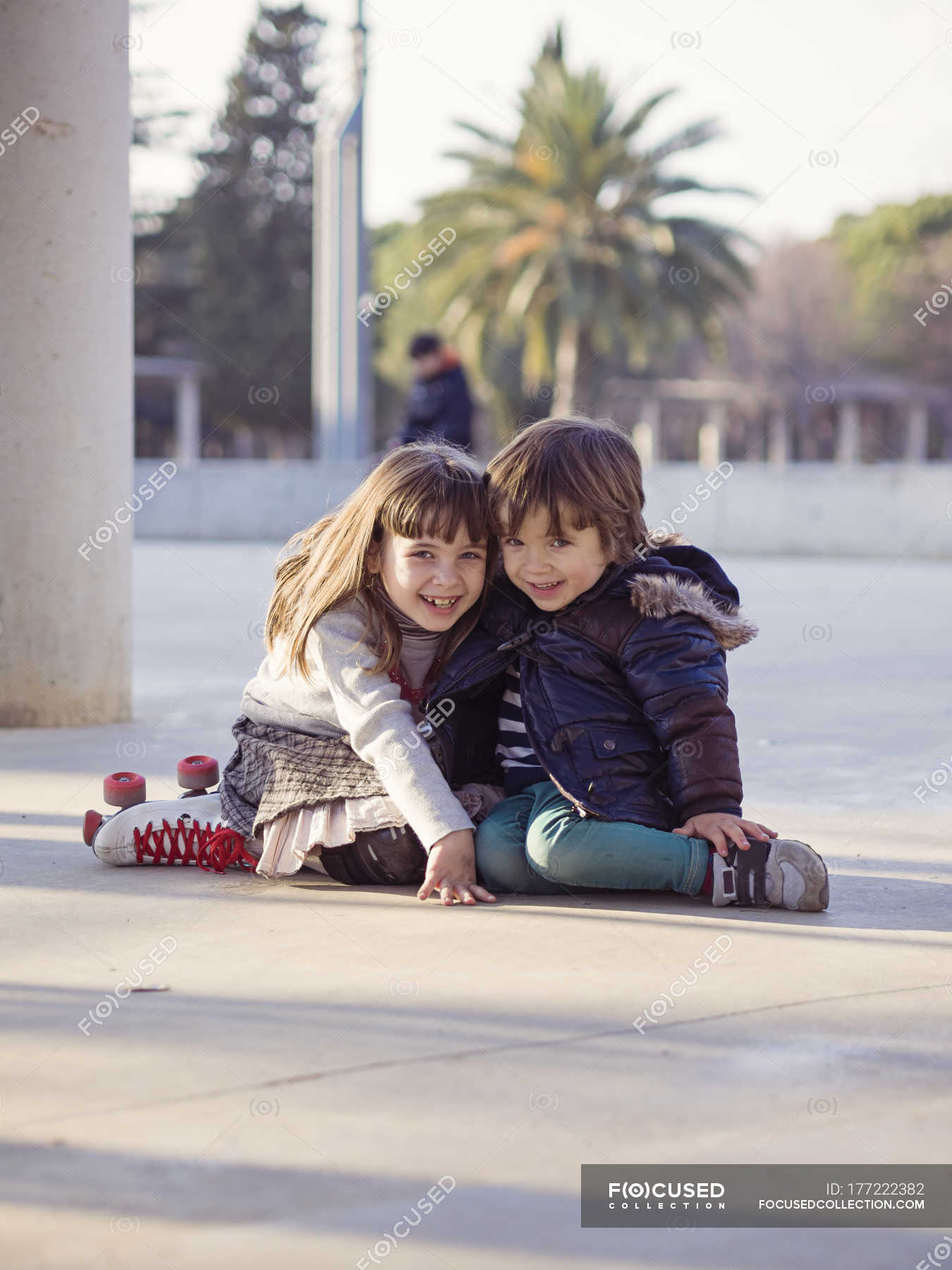 Smiling Little Boy And Girl Sitting Side By Side On The Ground In The City Sister Female Stock Photo