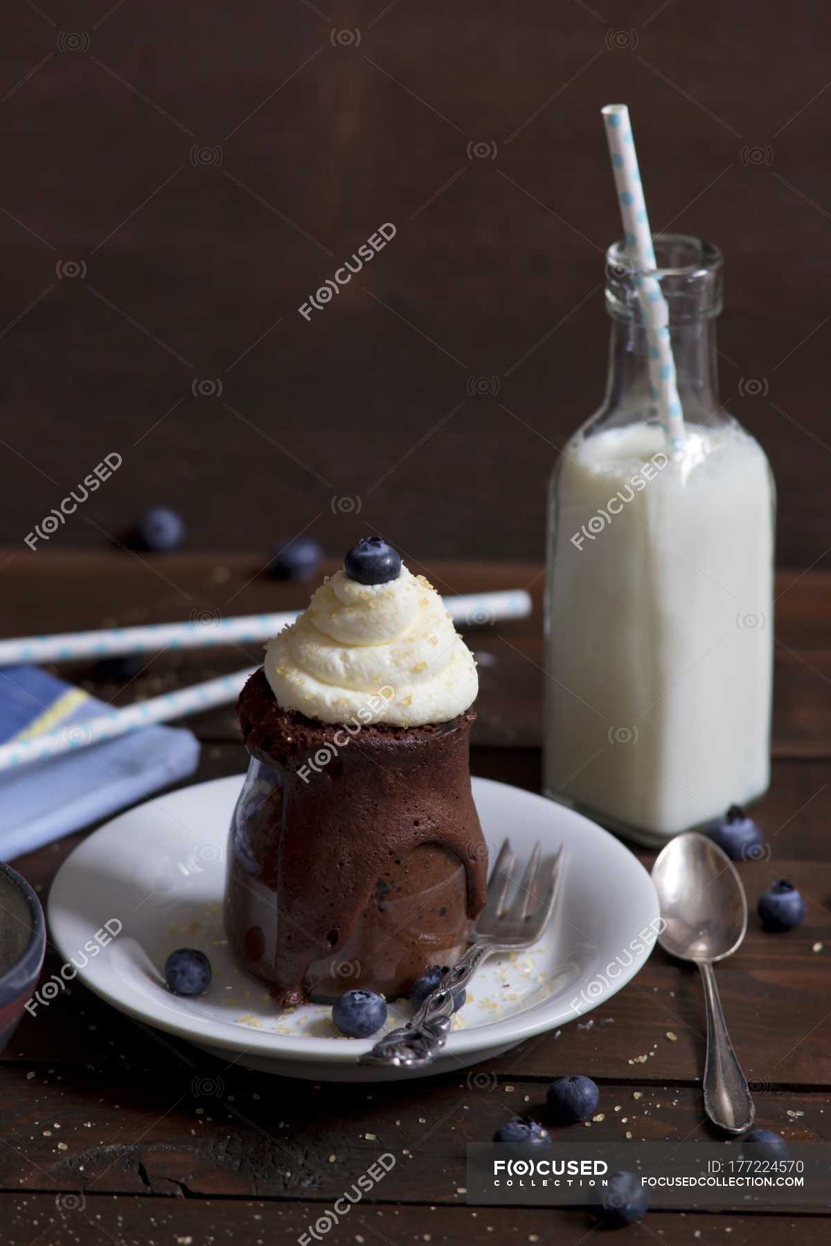 Chocolate cake in a glass with whipped cream, cane sugar and blueberries and a bottle of milk