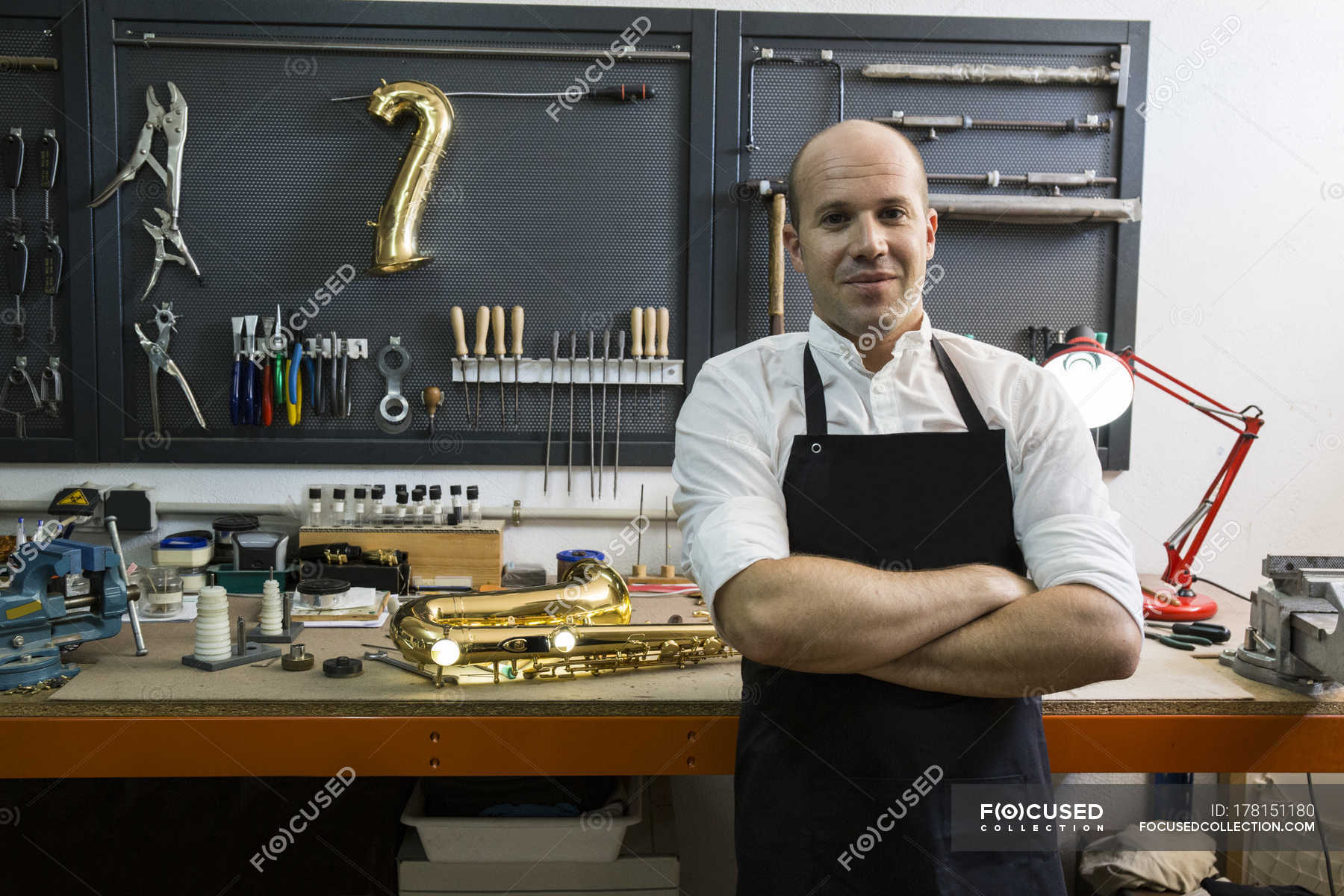 Instrument maker standing on workplace beside saxophone — half length