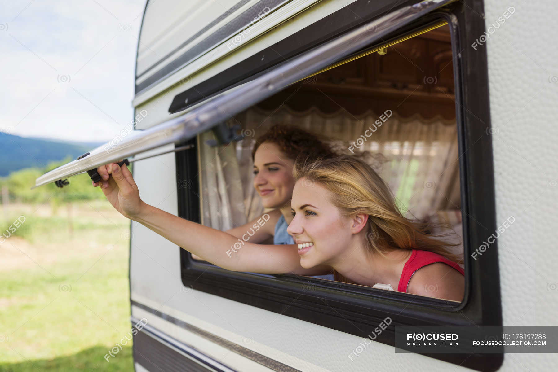 Two Female Friends Looking Through Window Of Caravan Color Image
