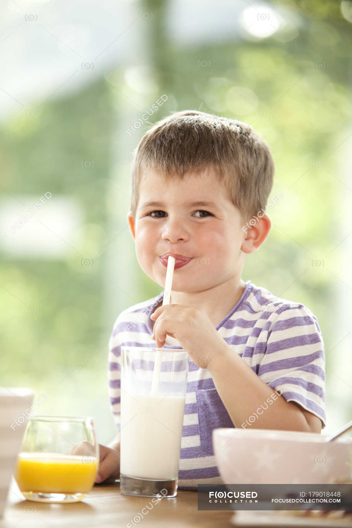 Boy drinking milk through silly straw glasses, while looking up Stock Photo