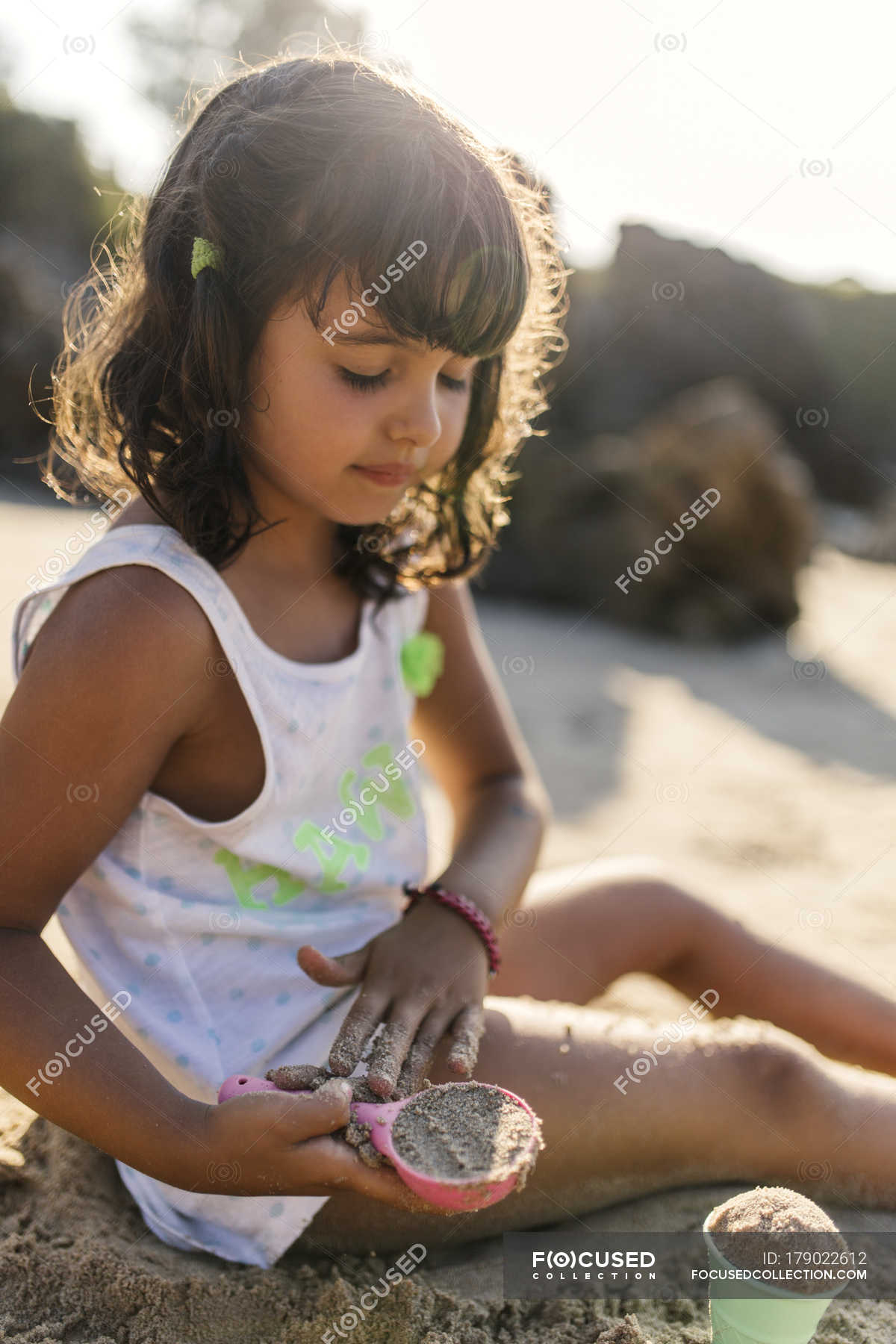 Petite fille jouant avec le sable sur la plage Cheveux foncés