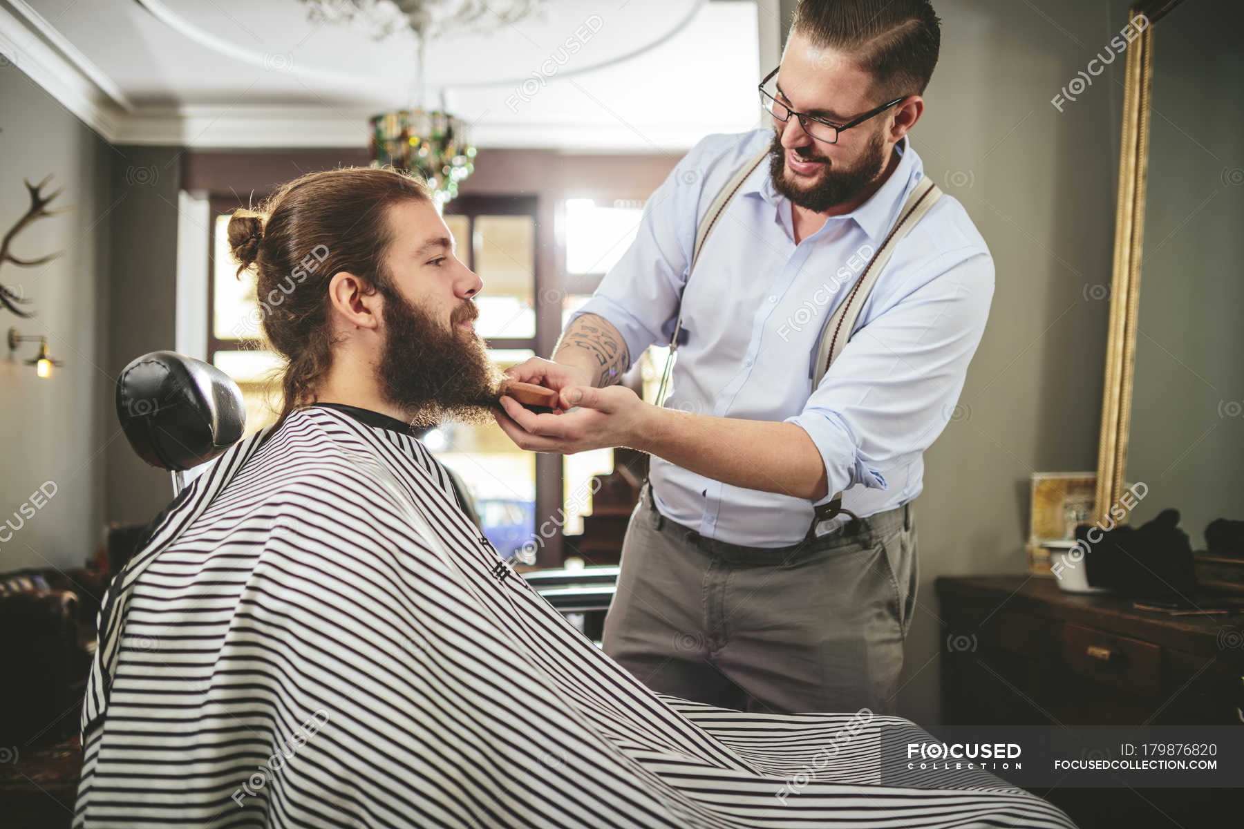 Barber brushing beard of a customer in barbershop — cape, smiling ...