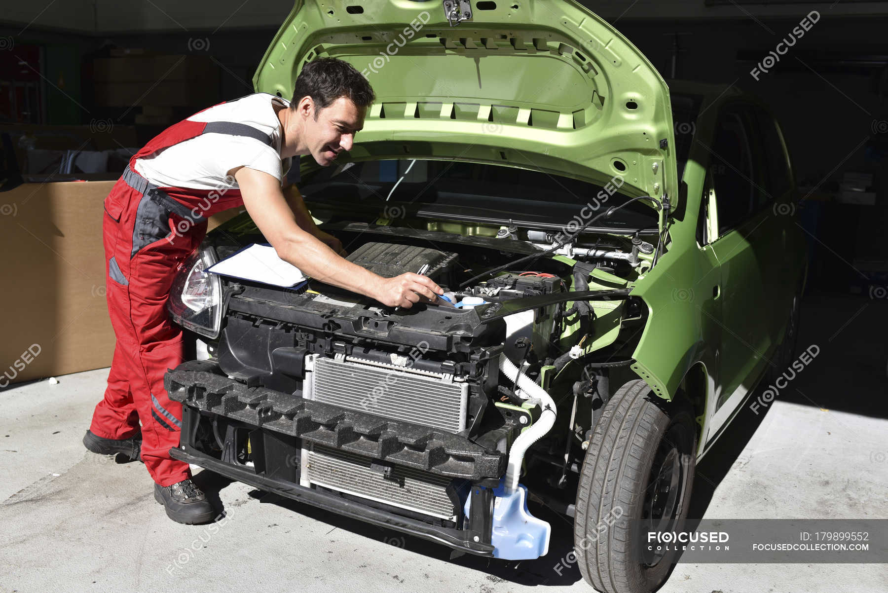 Car mechanic examining accident damaged car before repair — mid adult