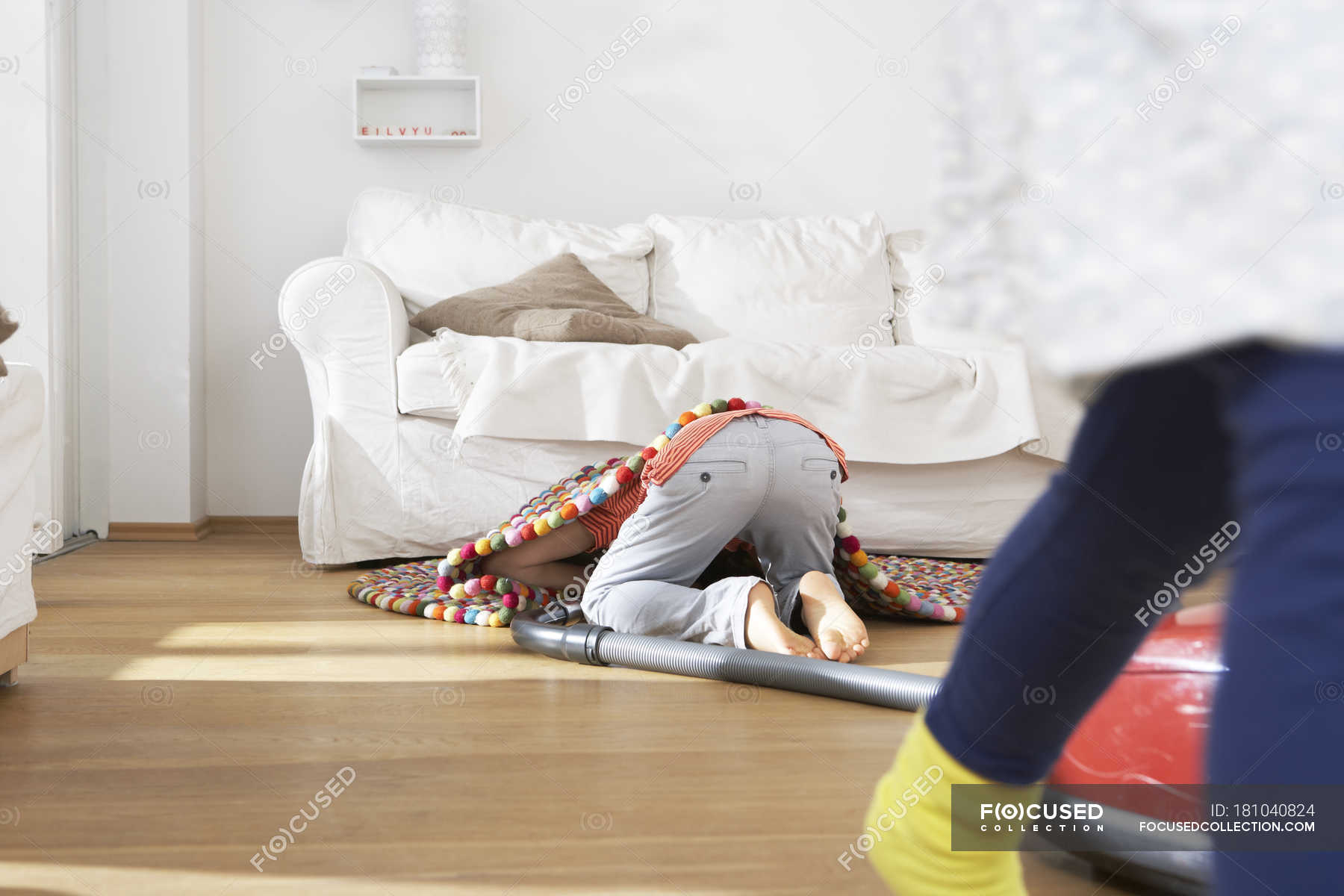 Boy in living room hoovering under carpet with girl walking on the