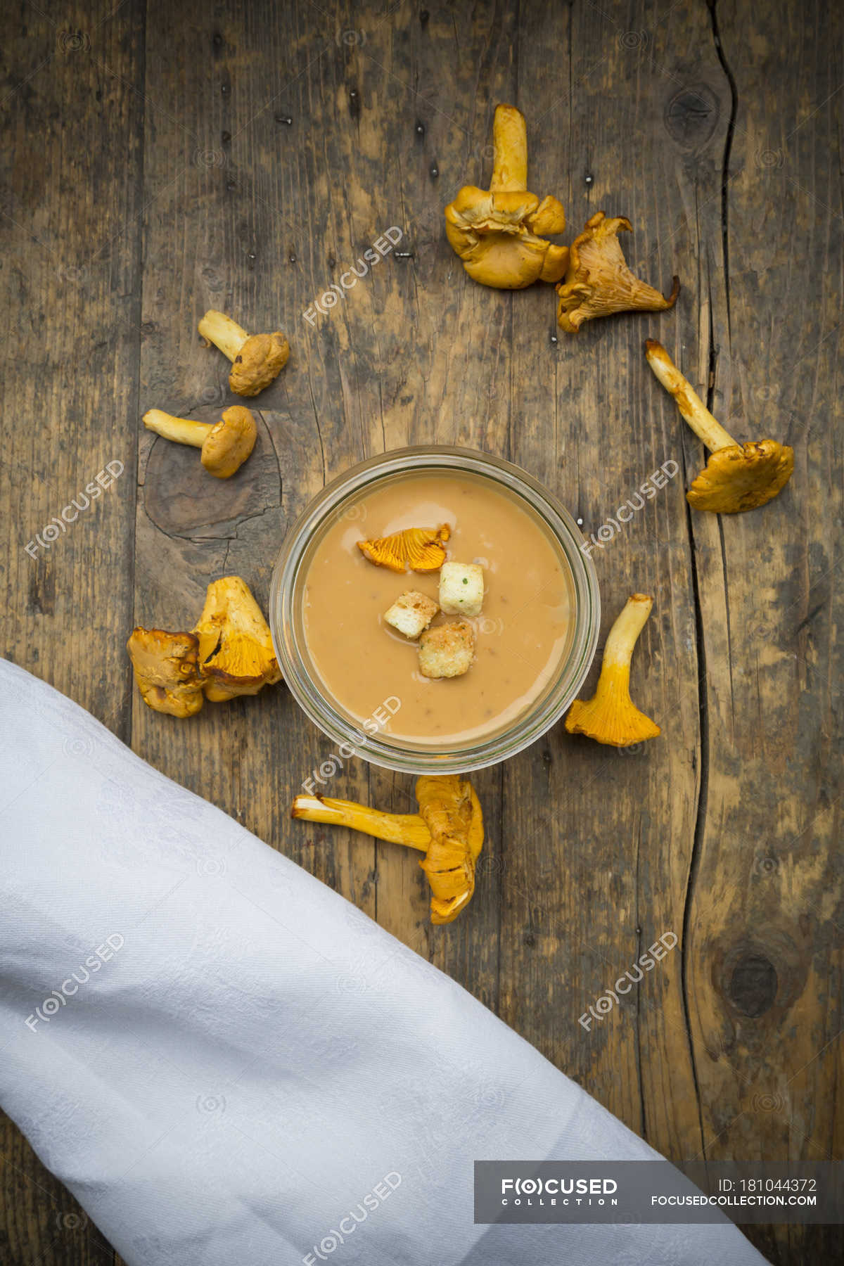 Bowl of cream of chanterelle soup, cloth and chanterelles on dark wood