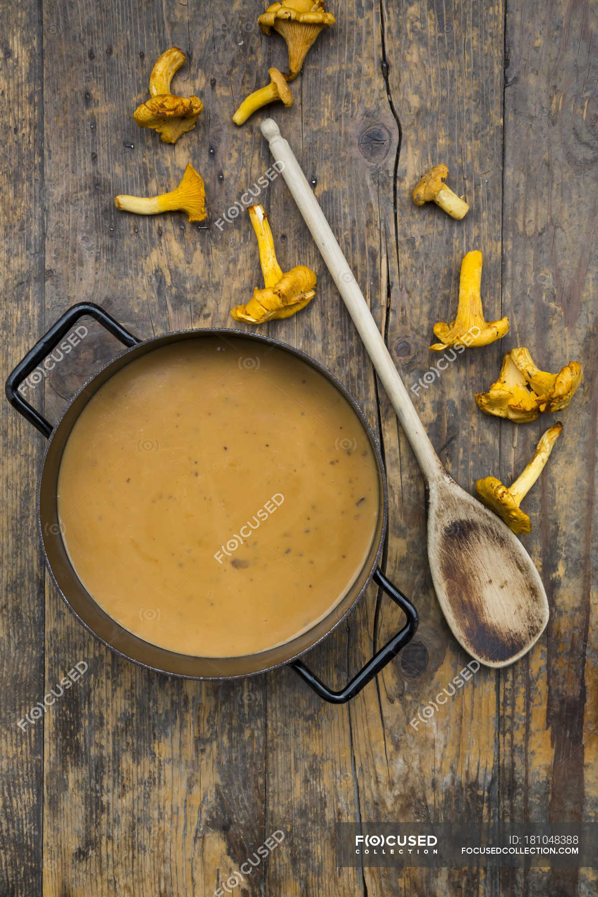 Cooking pot of cream of chanterelle soup, wooden spoon and chanterelles