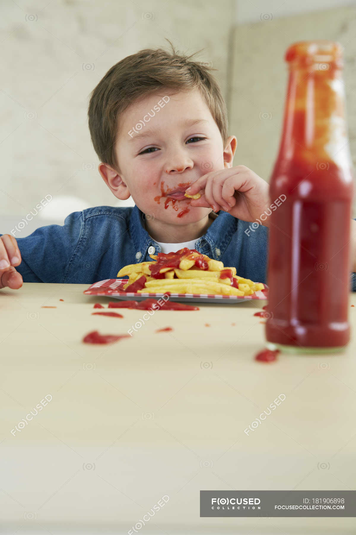 boy-eating-french-fries-with-ketchup-sauce-bottle-stock-photo