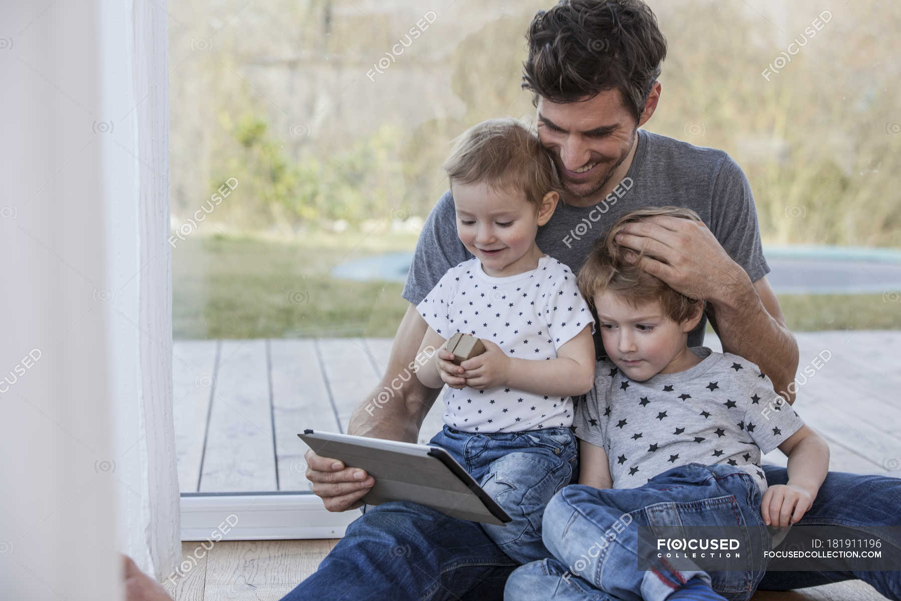 Father And Sons Sitting On Floor Using Digital Tablet Wireless Lan Smiling Stock Photo 181911196