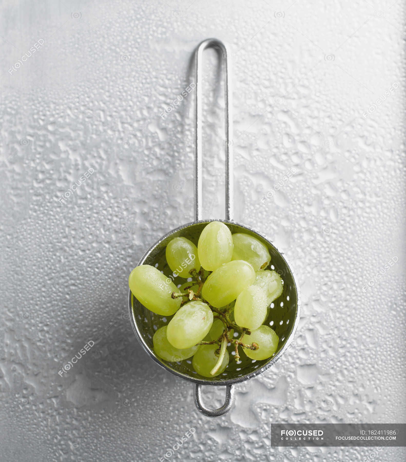 Fresh green grapes in strainer on metal surface with water drops