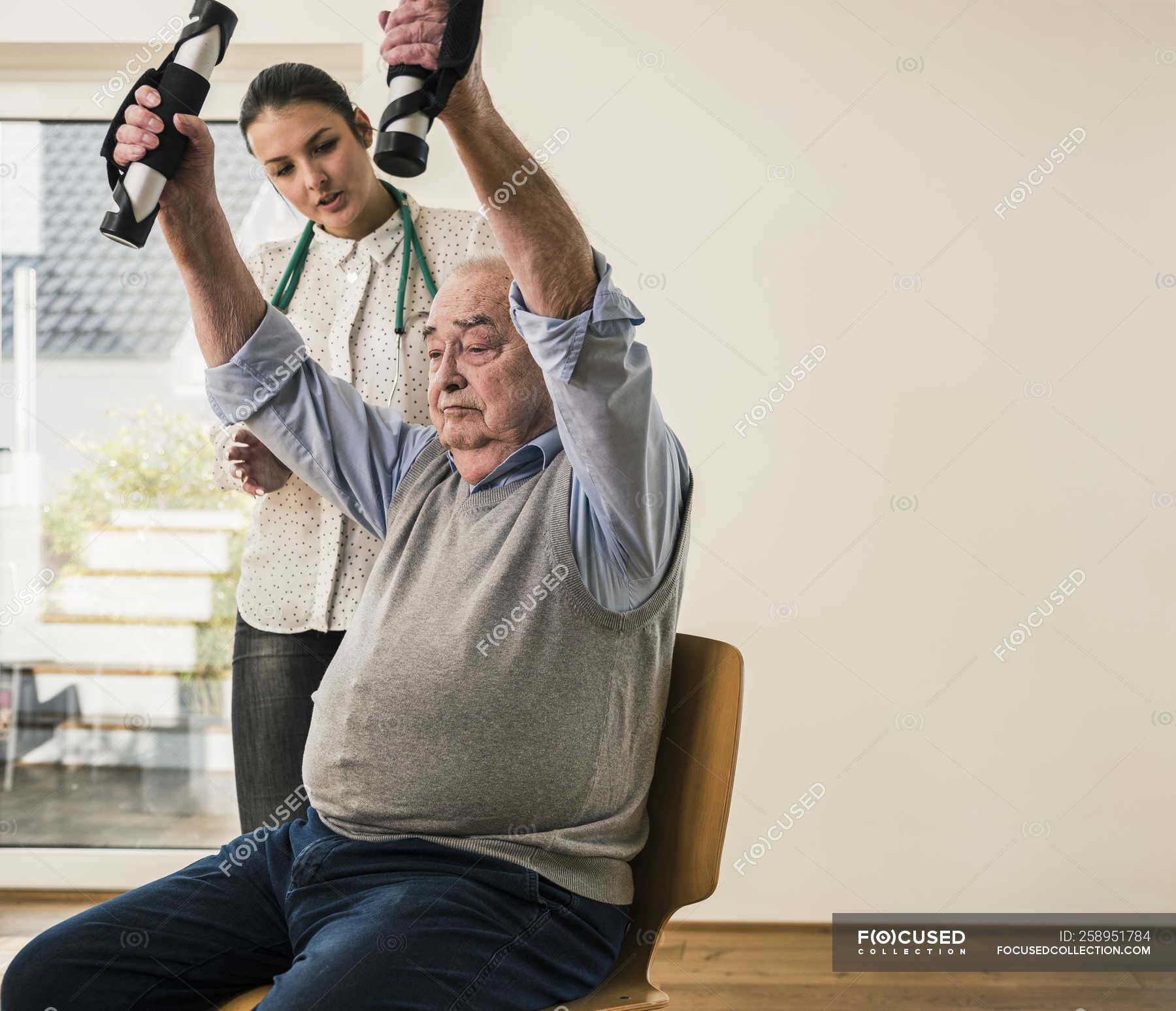 Young Woman Supporting Senior Man Doing An Arm Exercise — Dedication