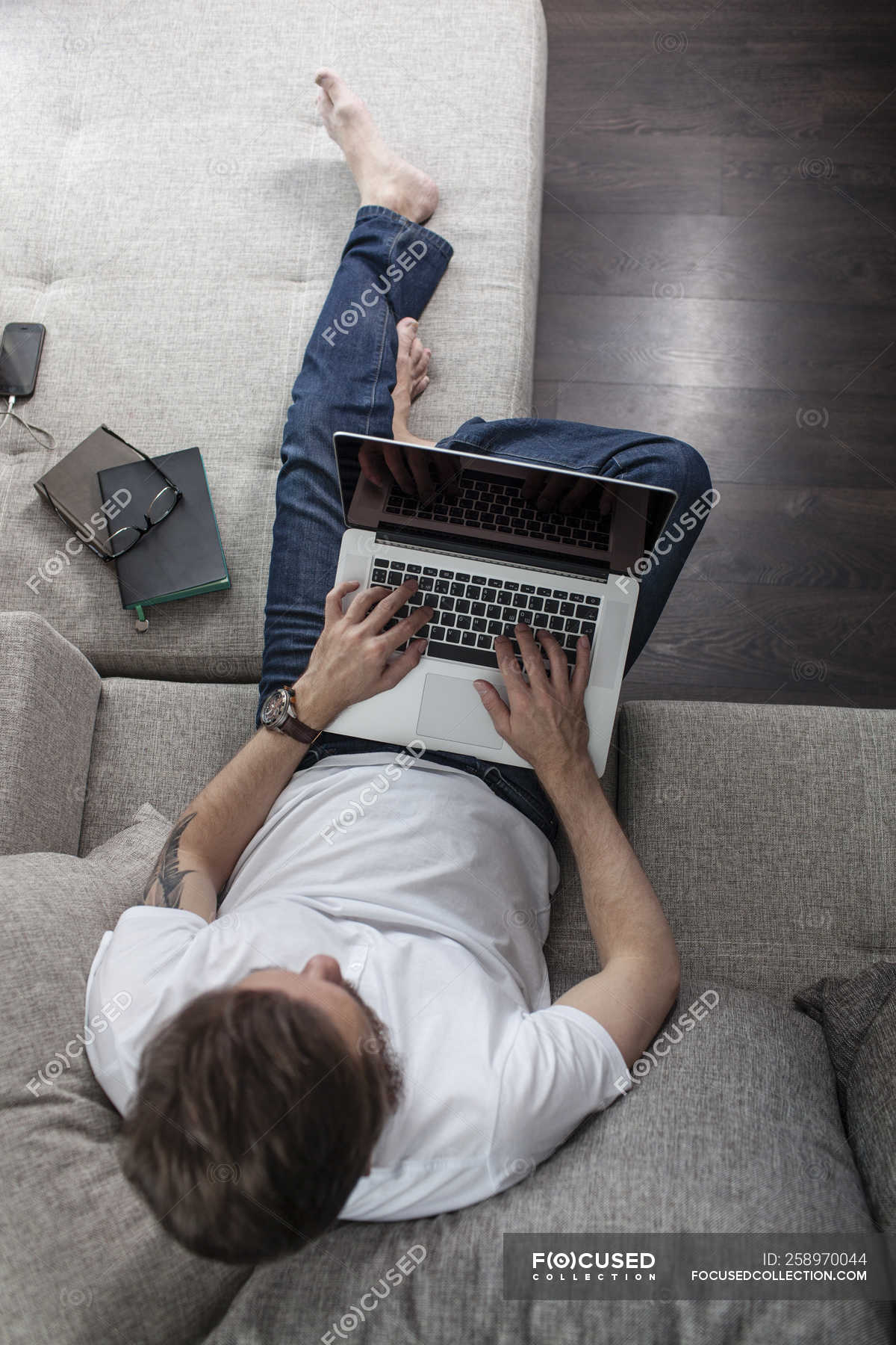 Мужчина сидит дома на диване и пользуется ноутбуком, вид сверху —мобильность, люди - Stock Photo