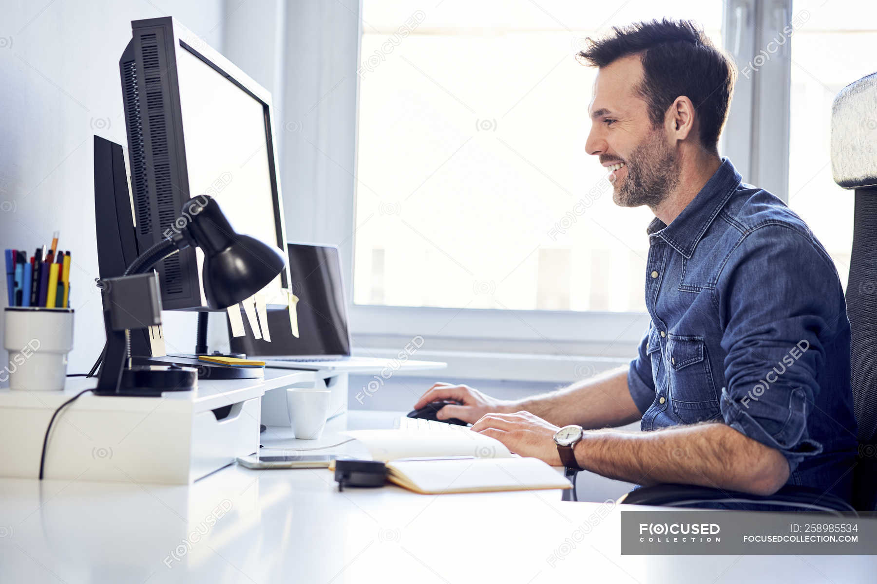 Smiling man working on computer at desk in office — casual, business