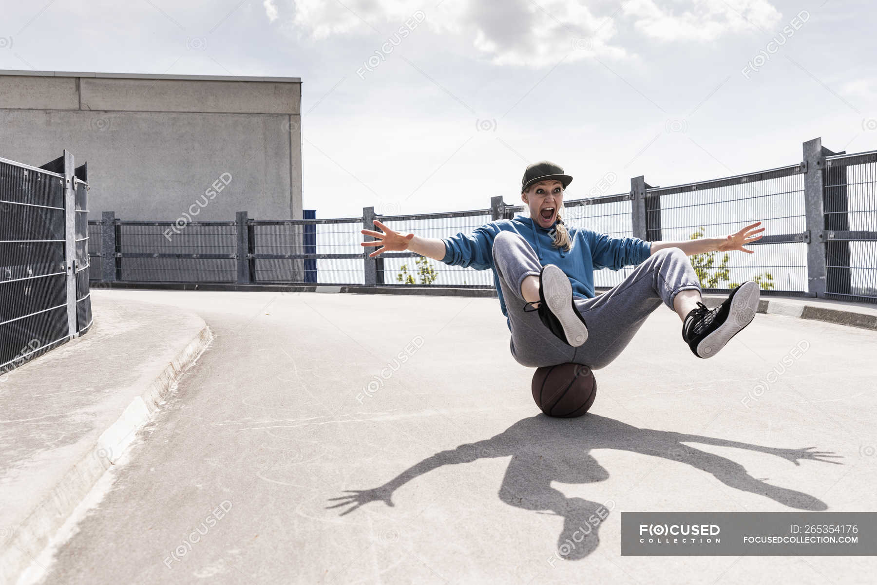 Woman sitting on basketball, rolling downhill — fit, day Stock Photo