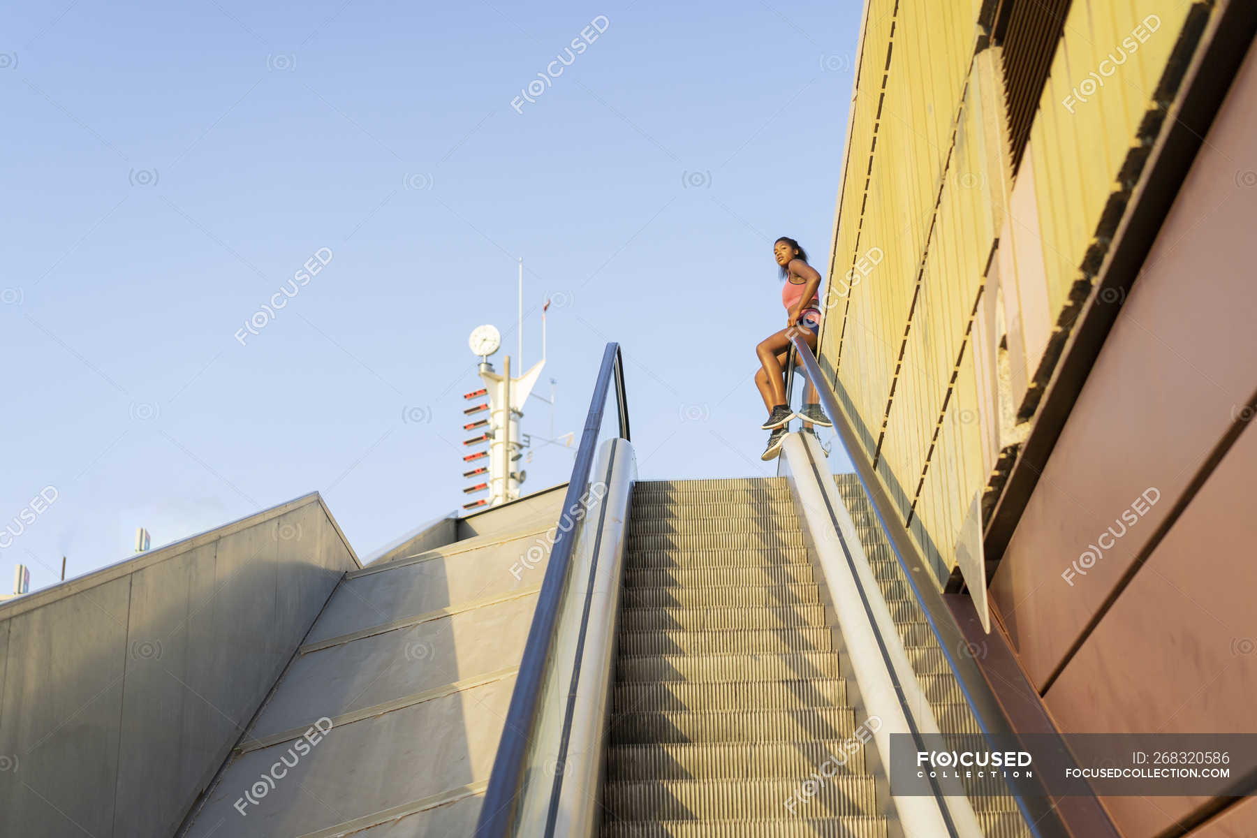 Young sportive woman sitting on escalator railing — recreational ...