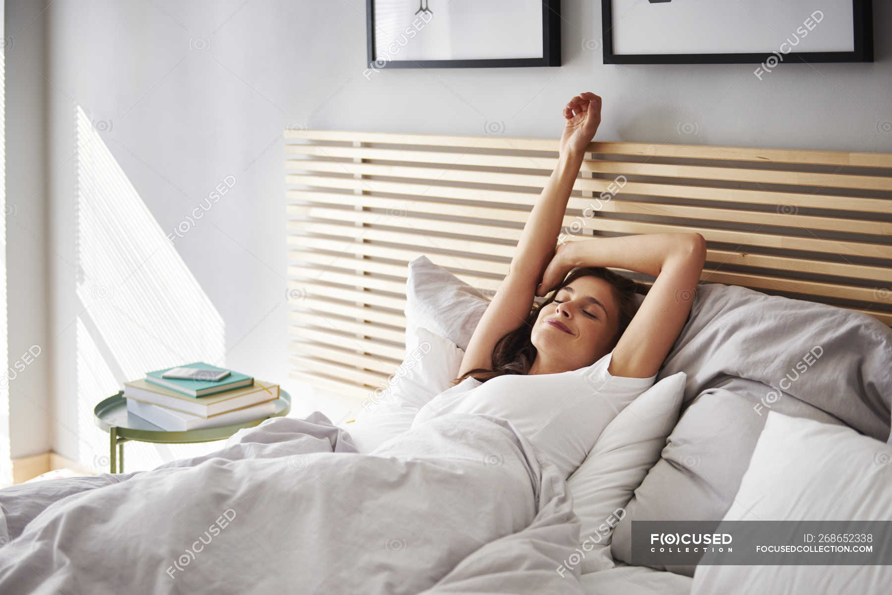 smiling-young-woman-relaxing-in-bed-outstretched-millennials-stock