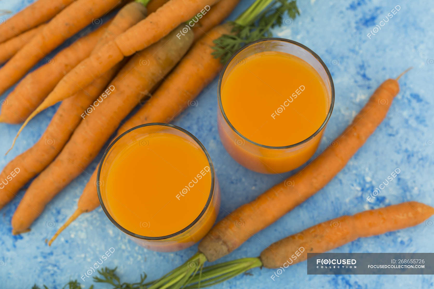 Two glasses of fresh carrot juice and carrots on light blue ground —  Elevated View, indoors - Stock Photo | #268655726