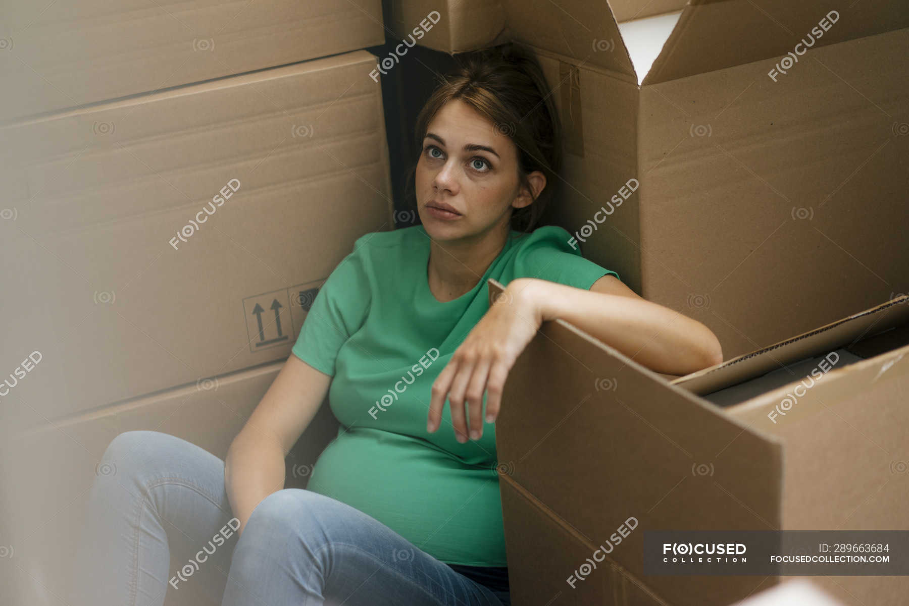 Exhausted pregnant woman sitting on floor surrounded by cardboard boxes