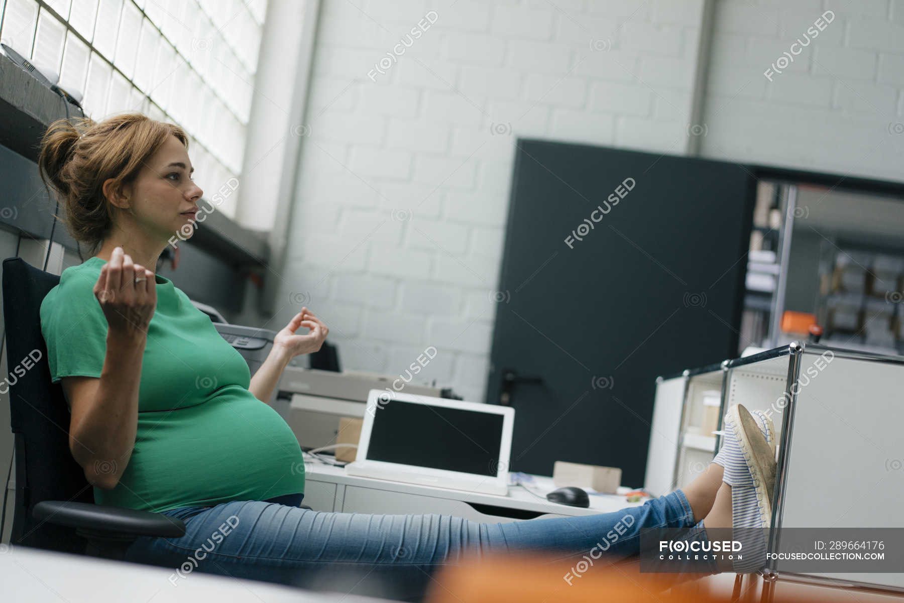 Pregnant woman sitting at desk in office having a break — employee