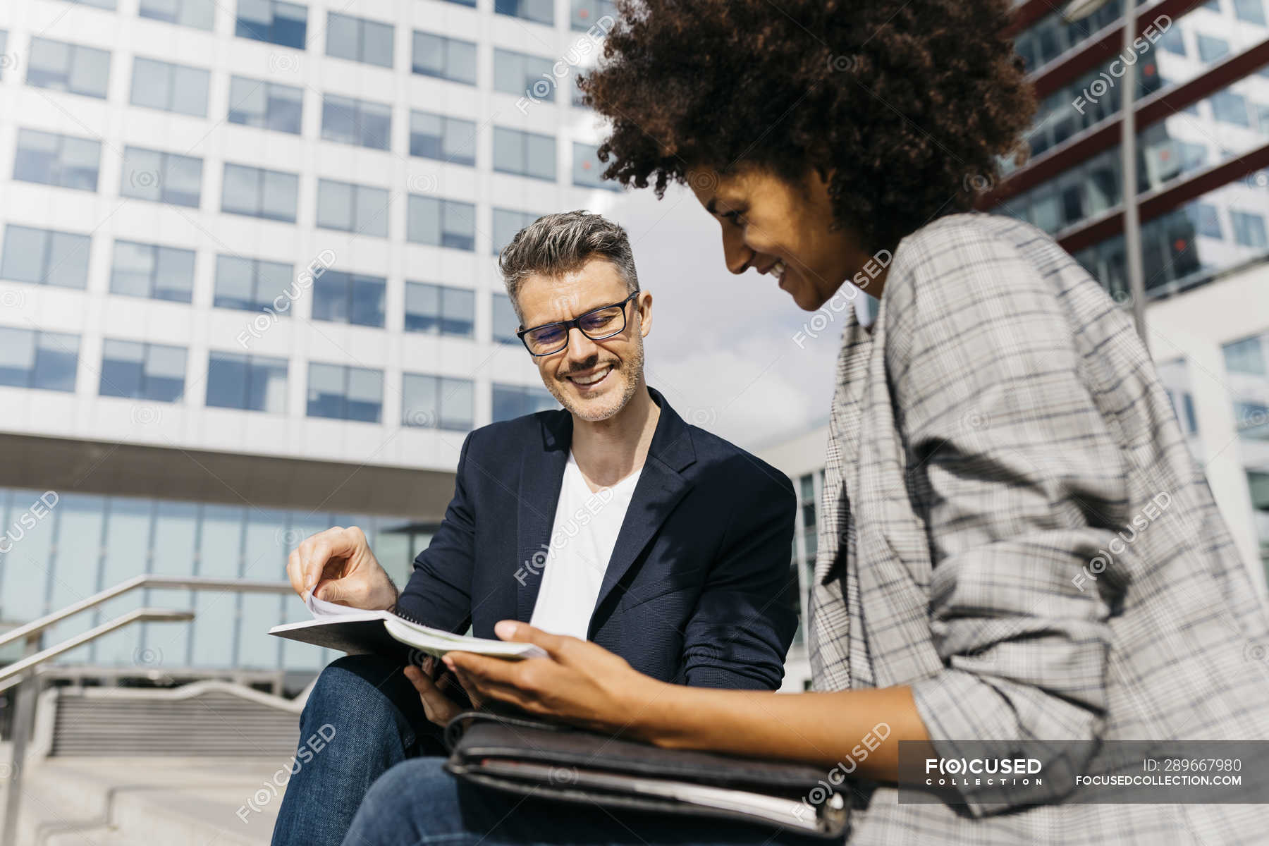 two-happy-colleagues-working-together-outside-office-building-sharing