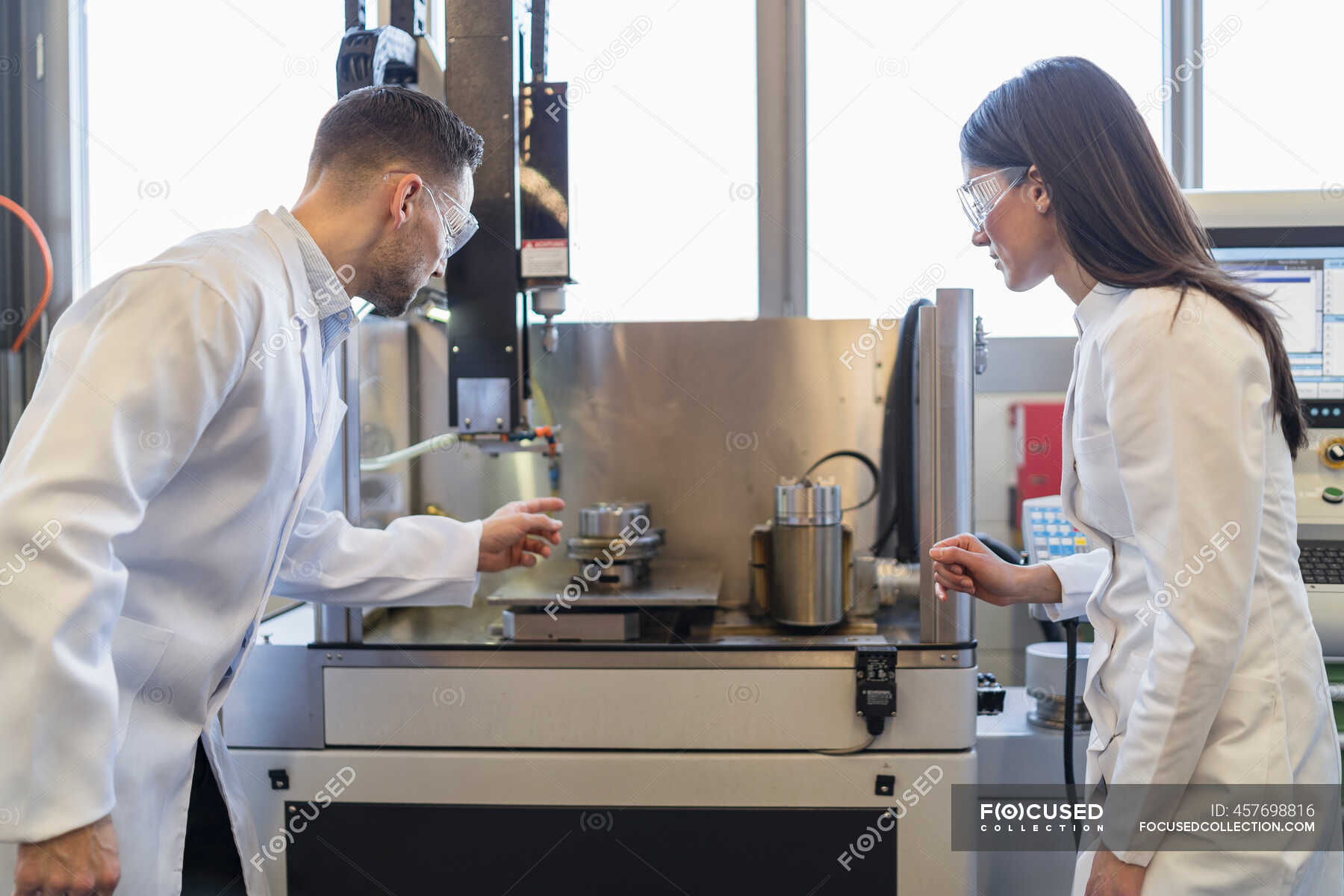 Colleagues wearing lab coats and safety goggles looking at machine in