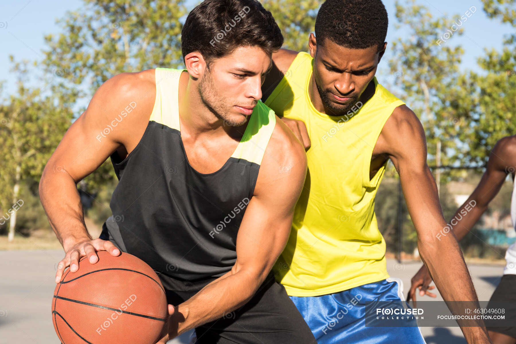 Young men playing basketball and dribbling ball on sports ground