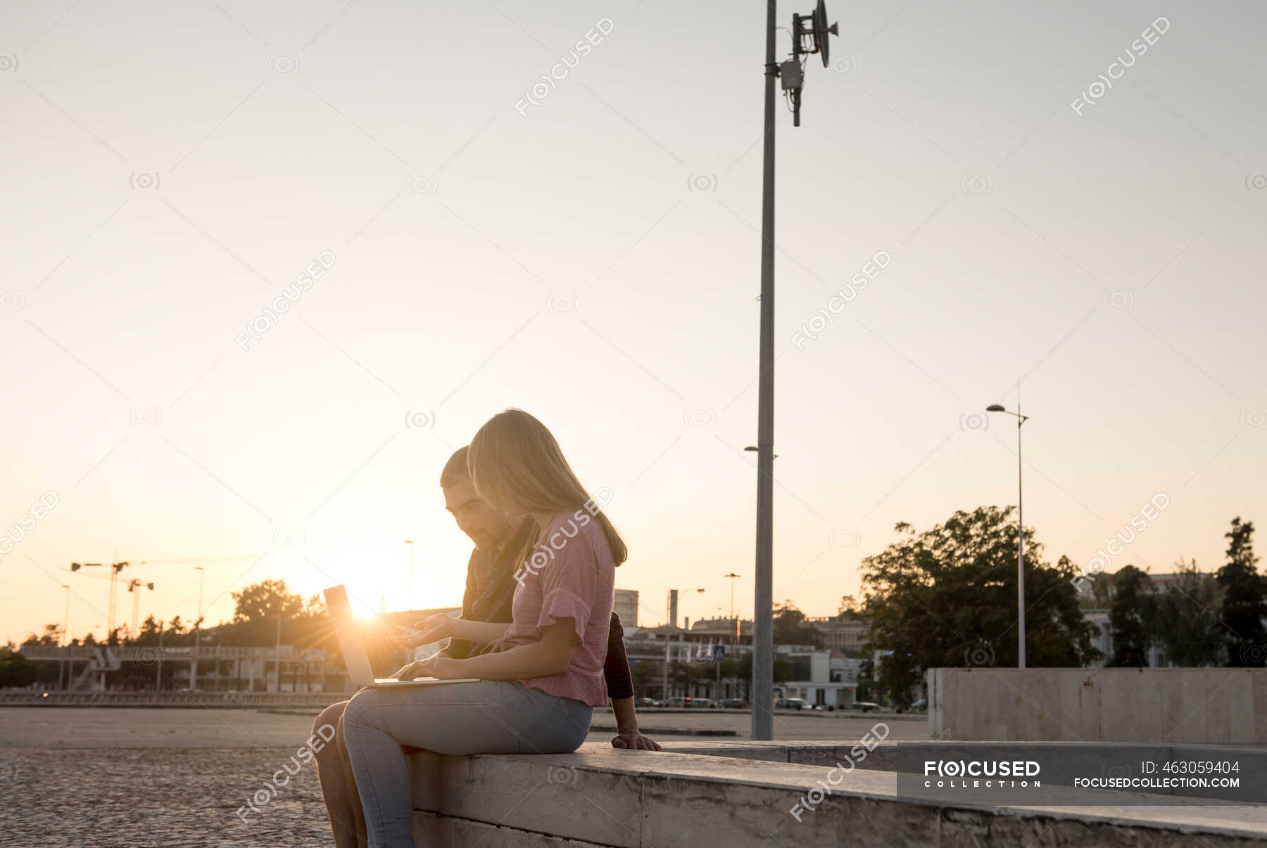 Man and woman using laptop outside in the sunset, Lisbon, Portugal