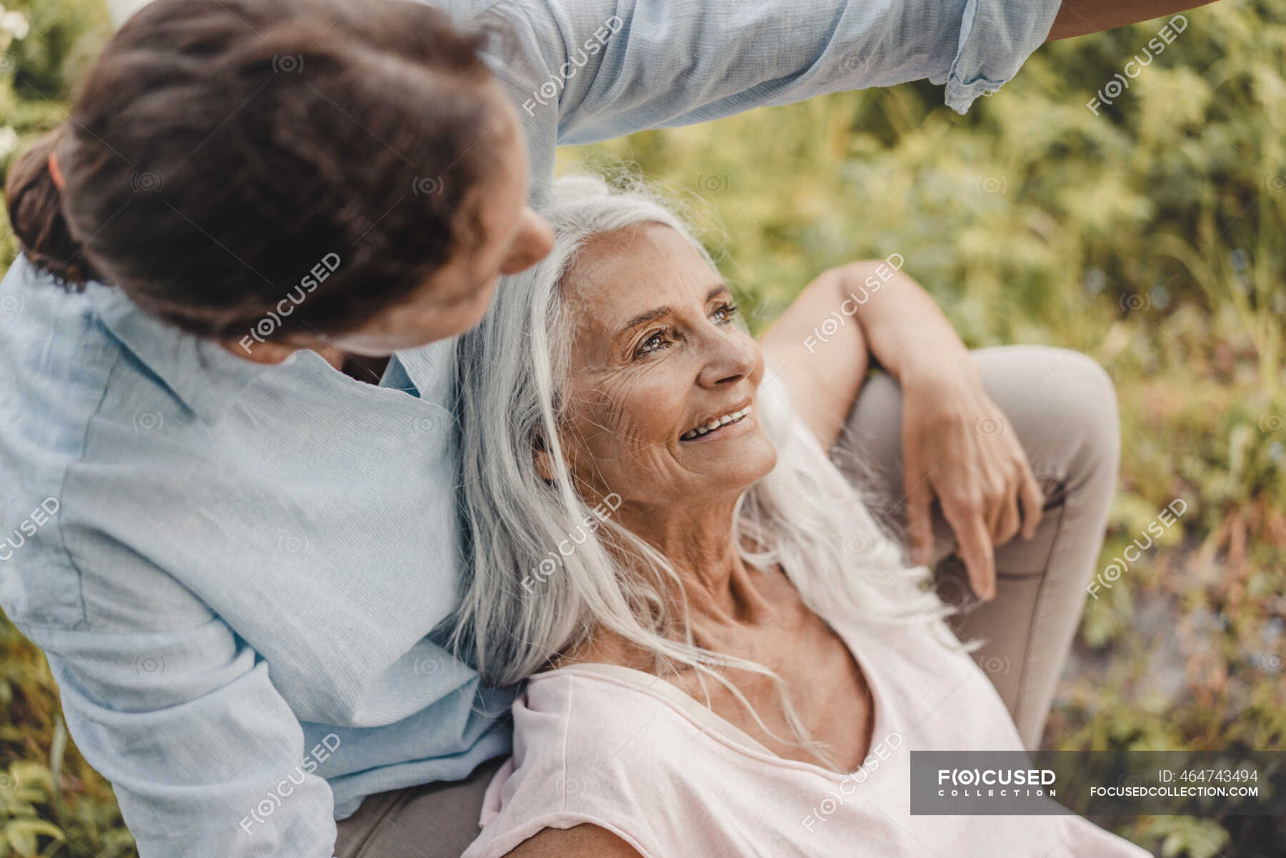 Daughter holding mother, leaning on lap, relaxing in nature — 60s