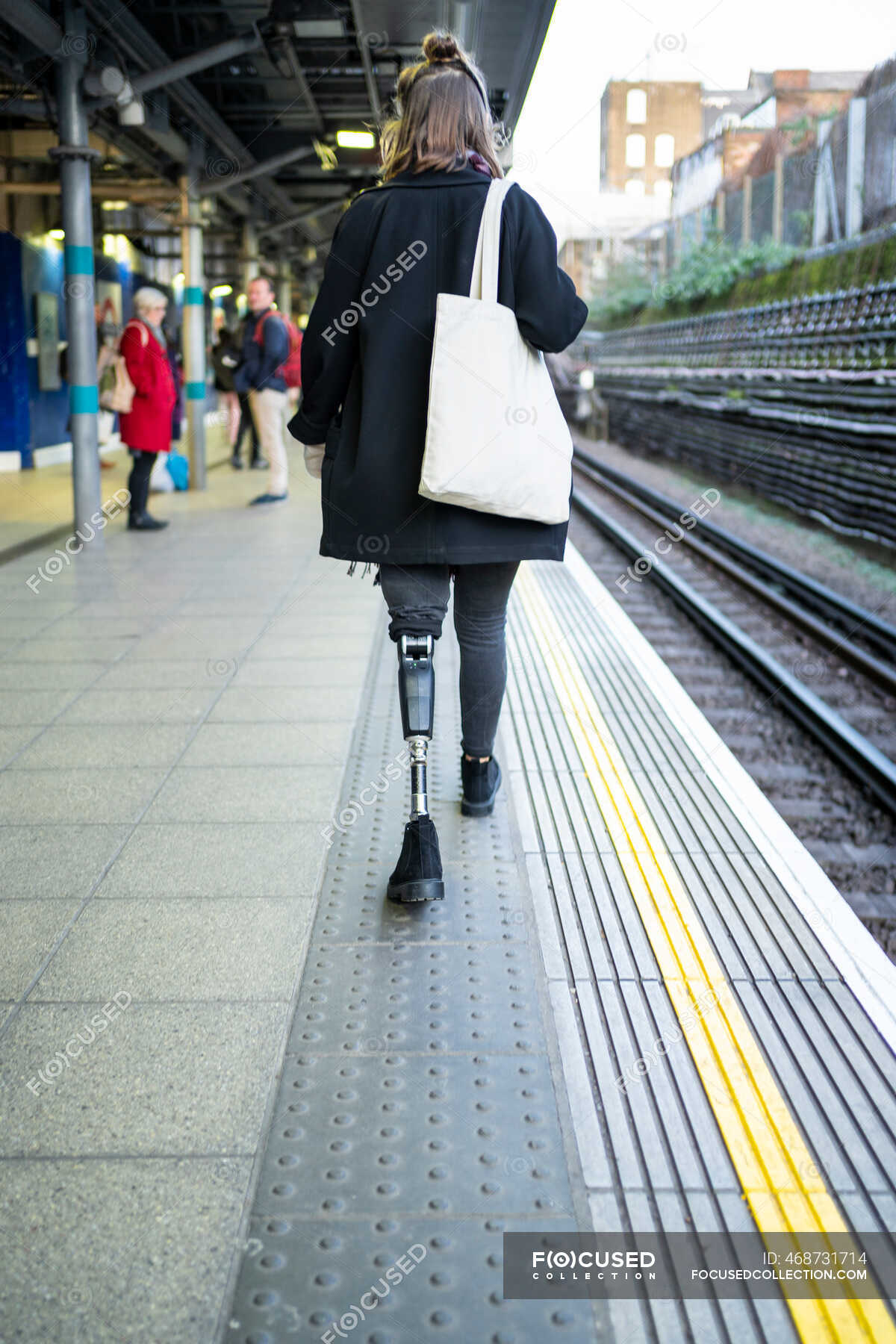 Vue arrière de la jeune femme avec prothèse de jambe marchant à la station platfom Navetteur