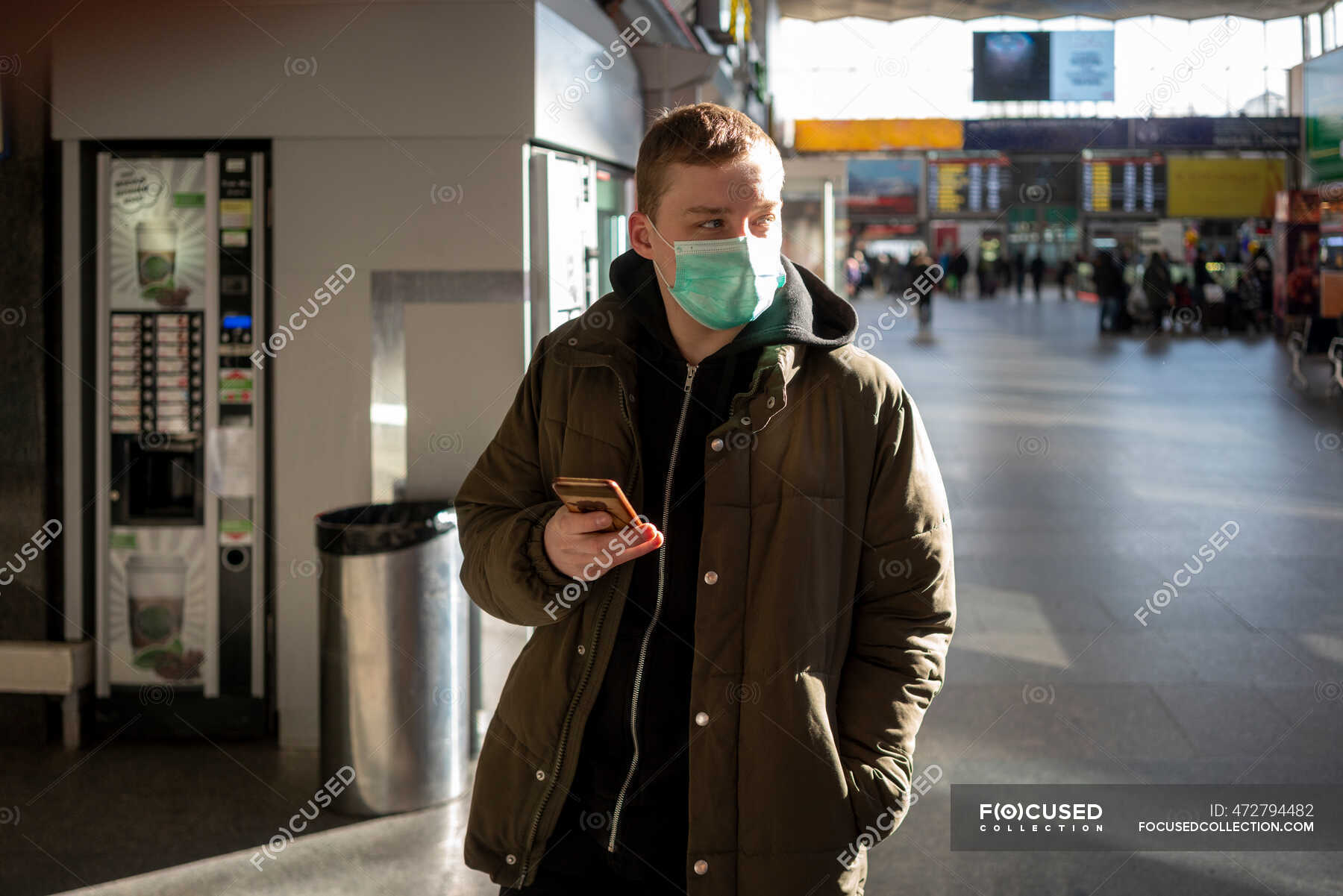 Young man with face mask at train station in the city, holding