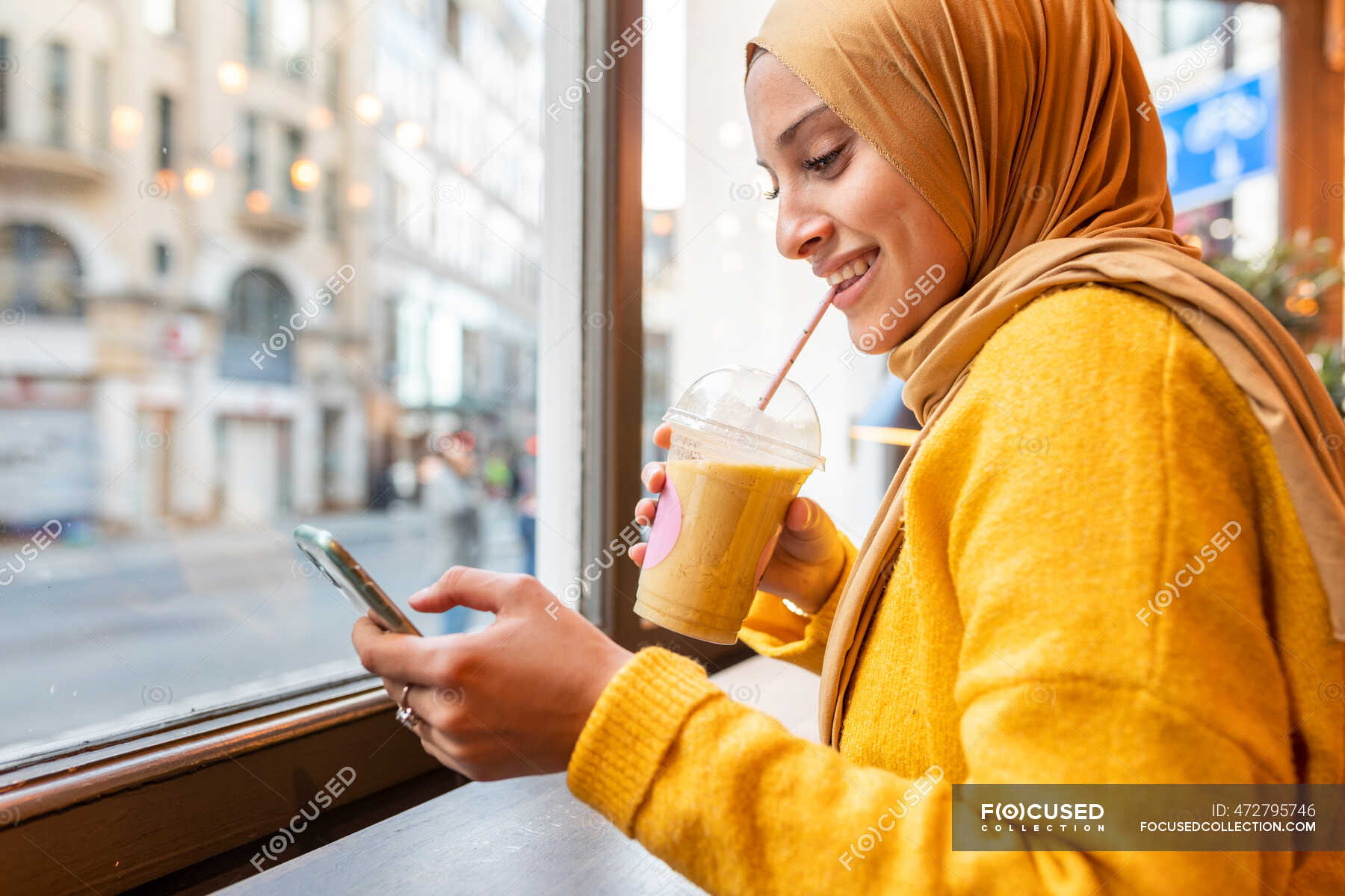 Portrait of happy young woman with smoothie and smartphone in a cafe —  muslim, Adults - Stock Photo | #472795746