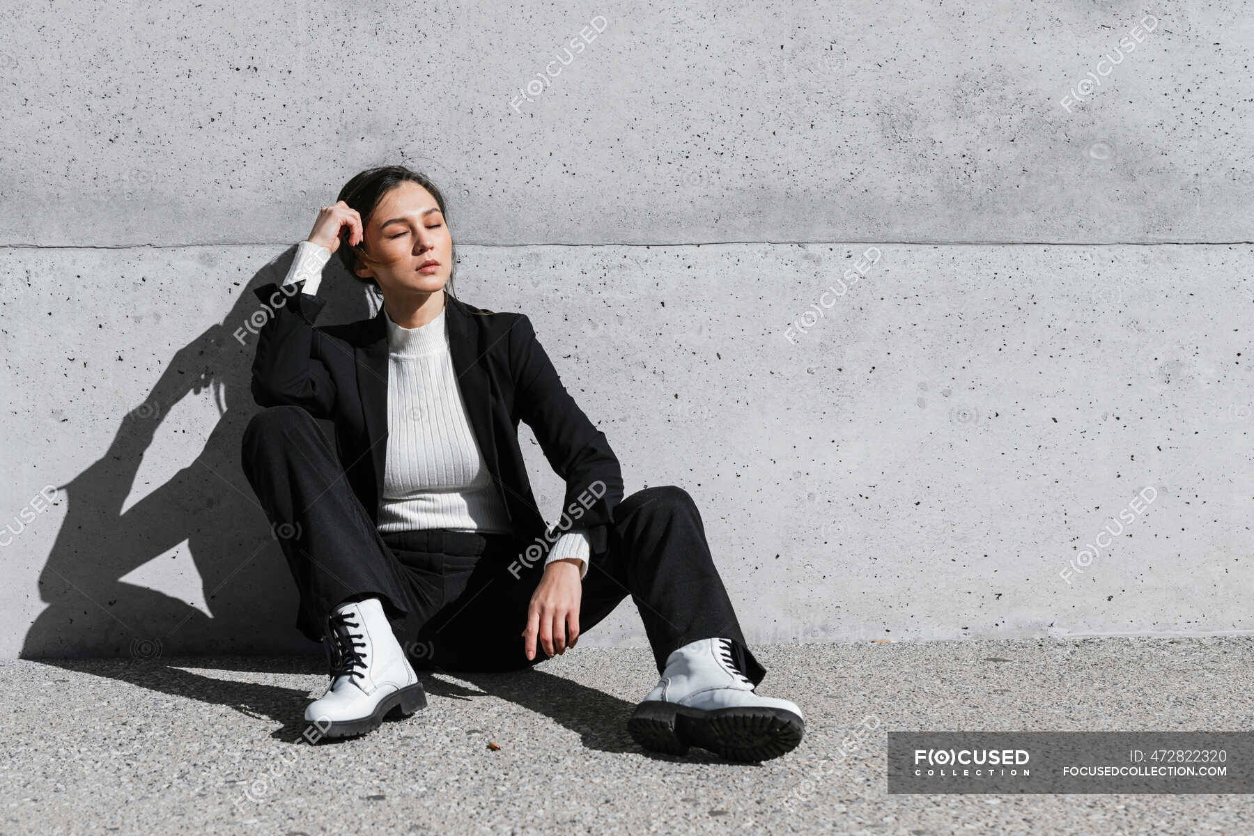 Young woman wearing black suit sitting on floor in front of concrete ...