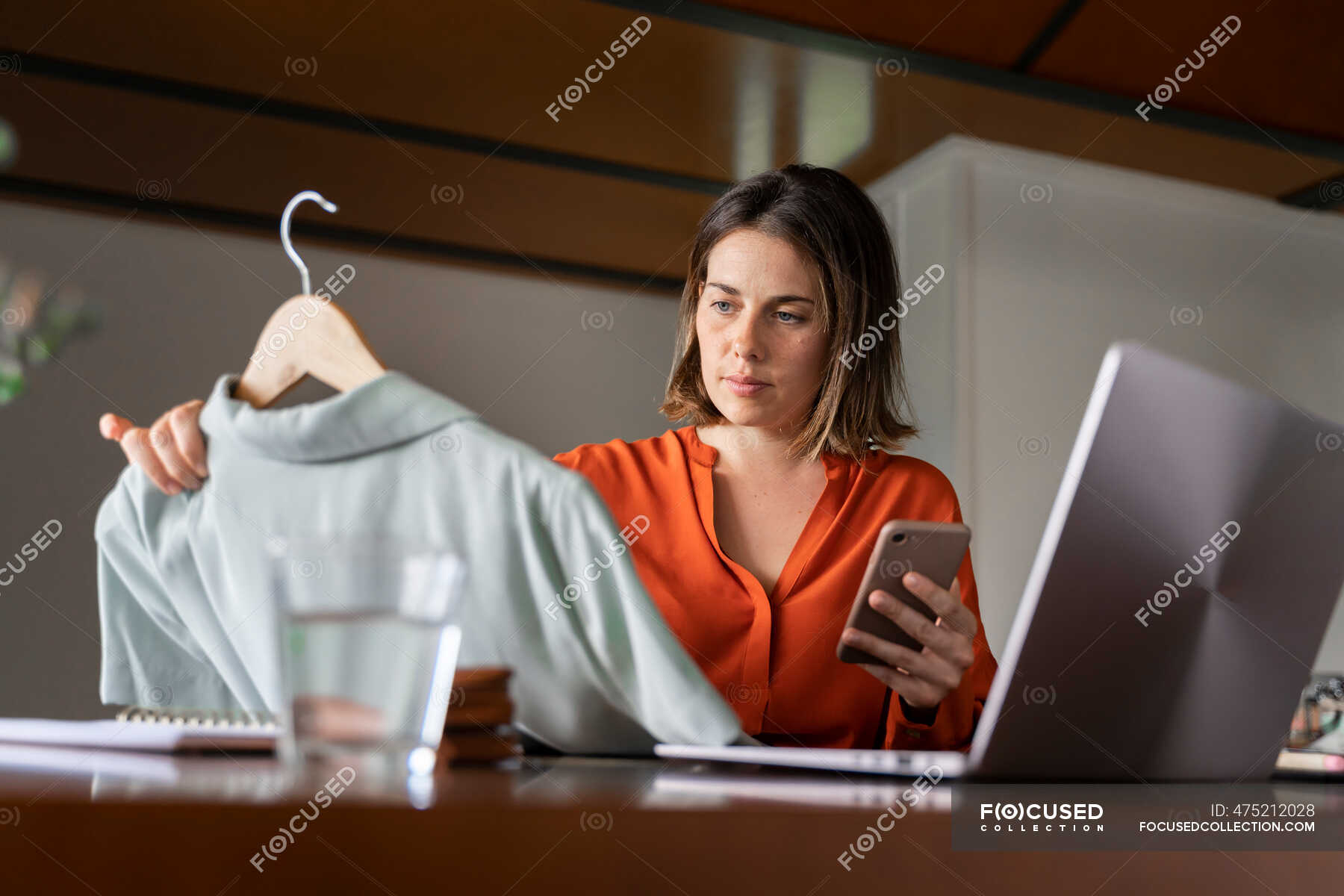 businesswoman-with-smart-phone-looking-at-clothes-while-sitting-at-home