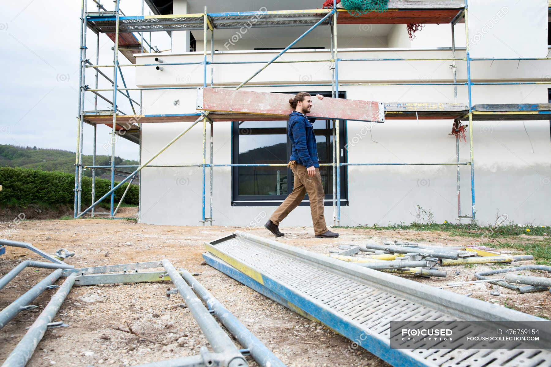 Construction worker carrying plank at construction site — building