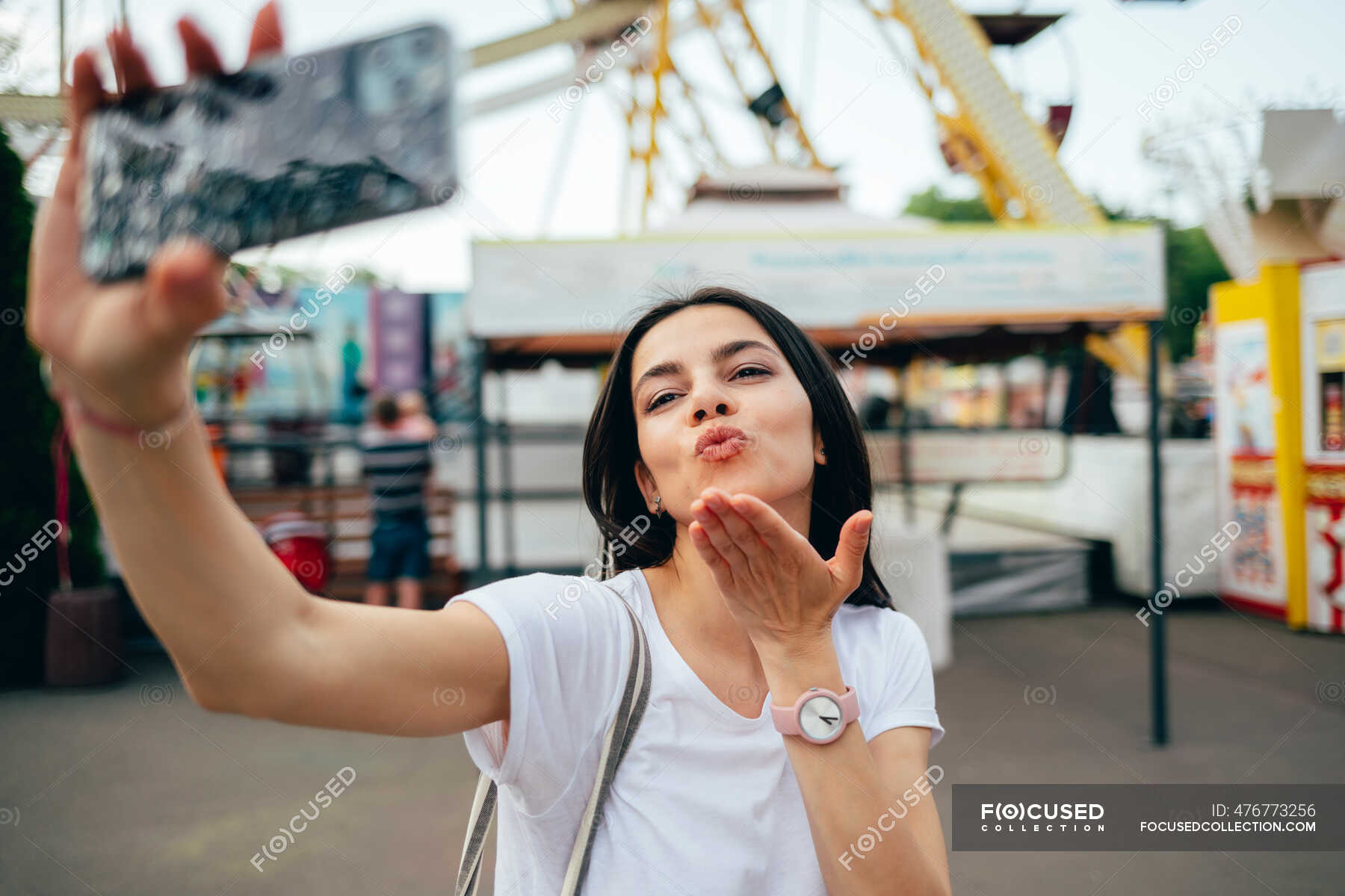 Young woman blowing kiss while taking selfie in amusement park ...