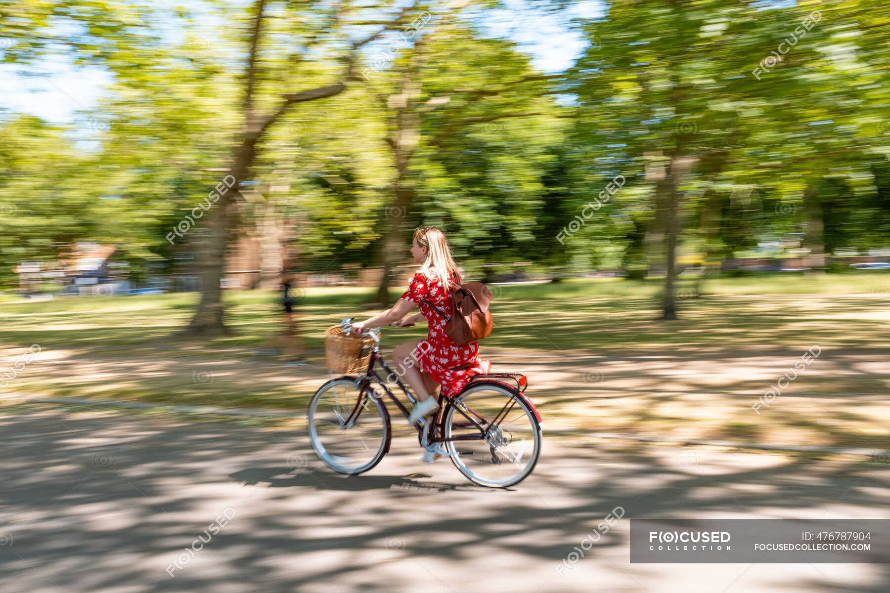 Blurred motion of woman riding bicycle on footpath at park — female
