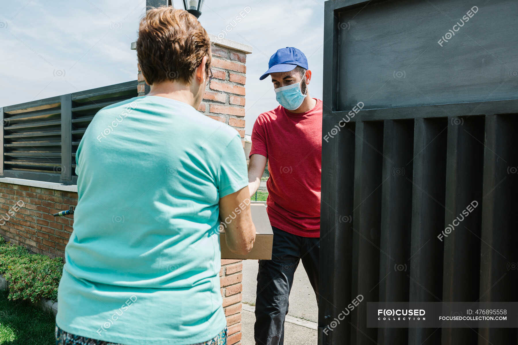 senior-woman-receiving-delivery-package-from-postal-worker-at-gate