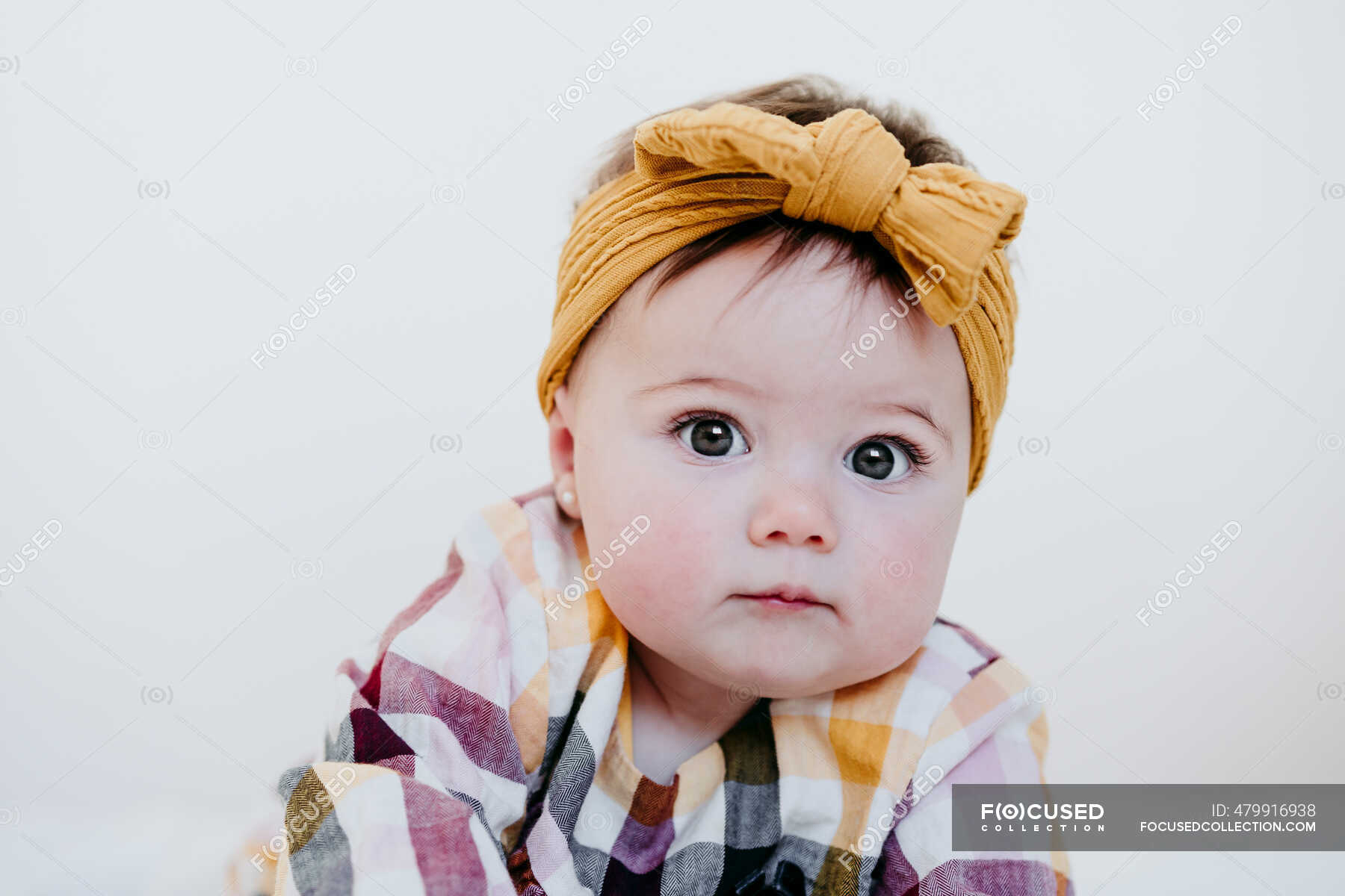 Baby girl wearing headband staring while lying on bed at home — yellow