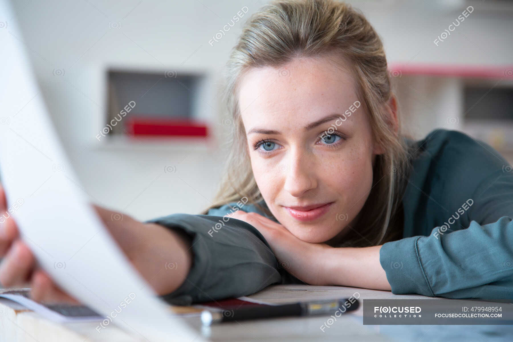 Portrait of woman leaning on desk in office holding paper — freelancer